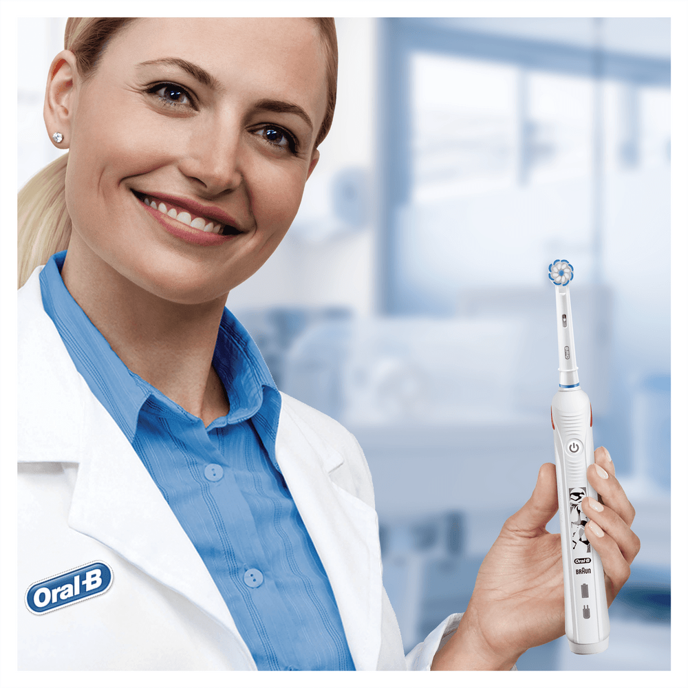 Una mujer con bata blanca sonríe, sosteniendo un cepillo dental eléctrico Oral-B.