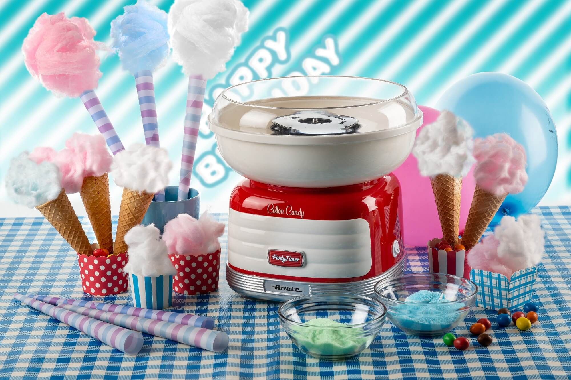 Zuckerwattemaschine mit Tüten, Süßigkeiten und Dekorationen auf einer karierten Tischdecke.