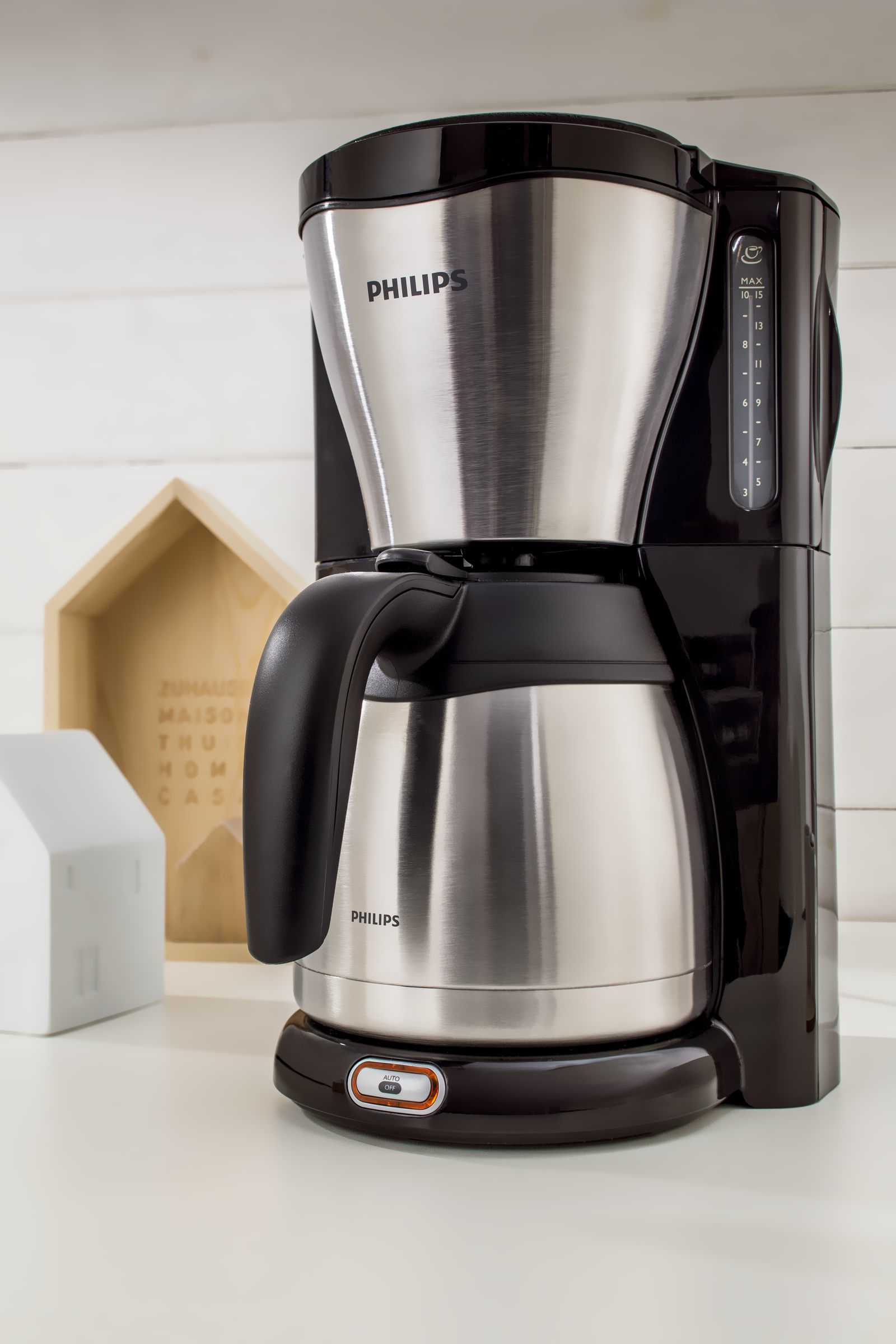Schwarze und silberne Philips Kaffeemaschine auf weißer Oberfläche. Holzhäuser im Hintergrund.