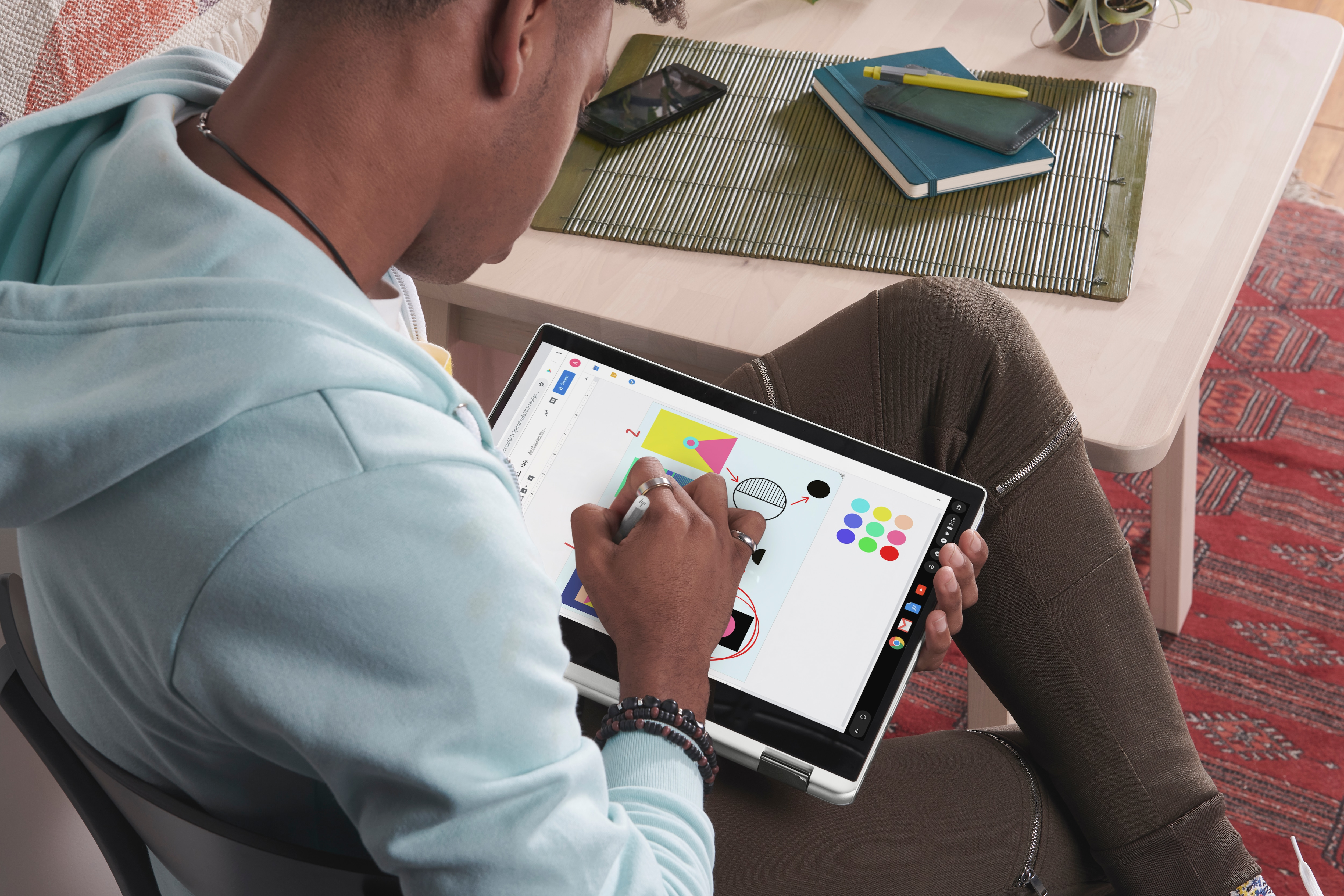 Eine Person benutzt ein Tablet, zeichnet mit einem Stift auf dem Bildschirm, sitzt am Tisch.