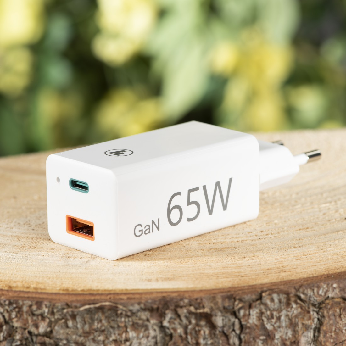 Weißes 65W GaN-Ladegerät mit USB-C- und USB-Anschluss auf Holz mit unscharfem Hintergrund.
