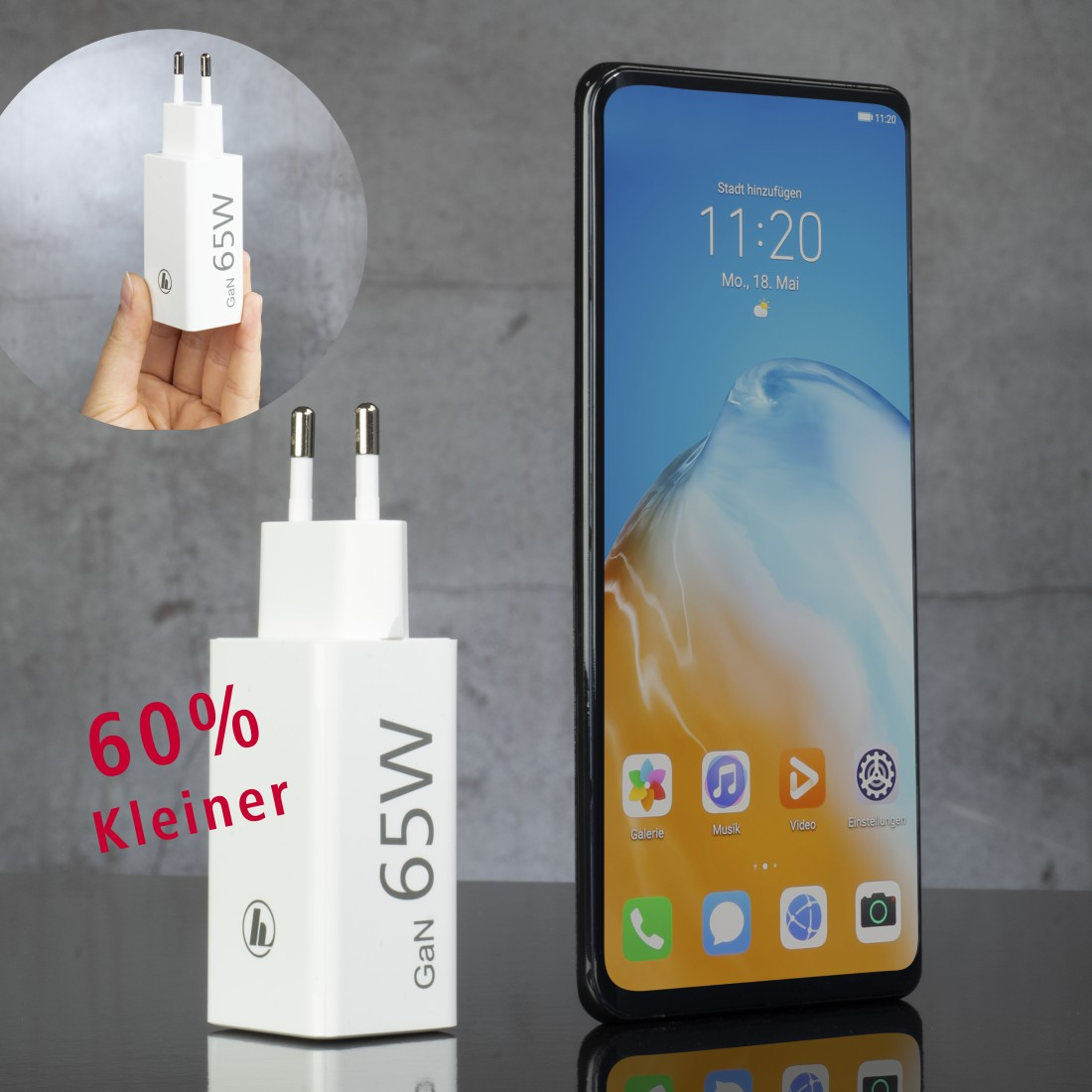 Ein weißes 65W-Ladegerät mit einem Telefon, das Zeit und Apps anzeigt. Eine Hand hält das Ladegerät.