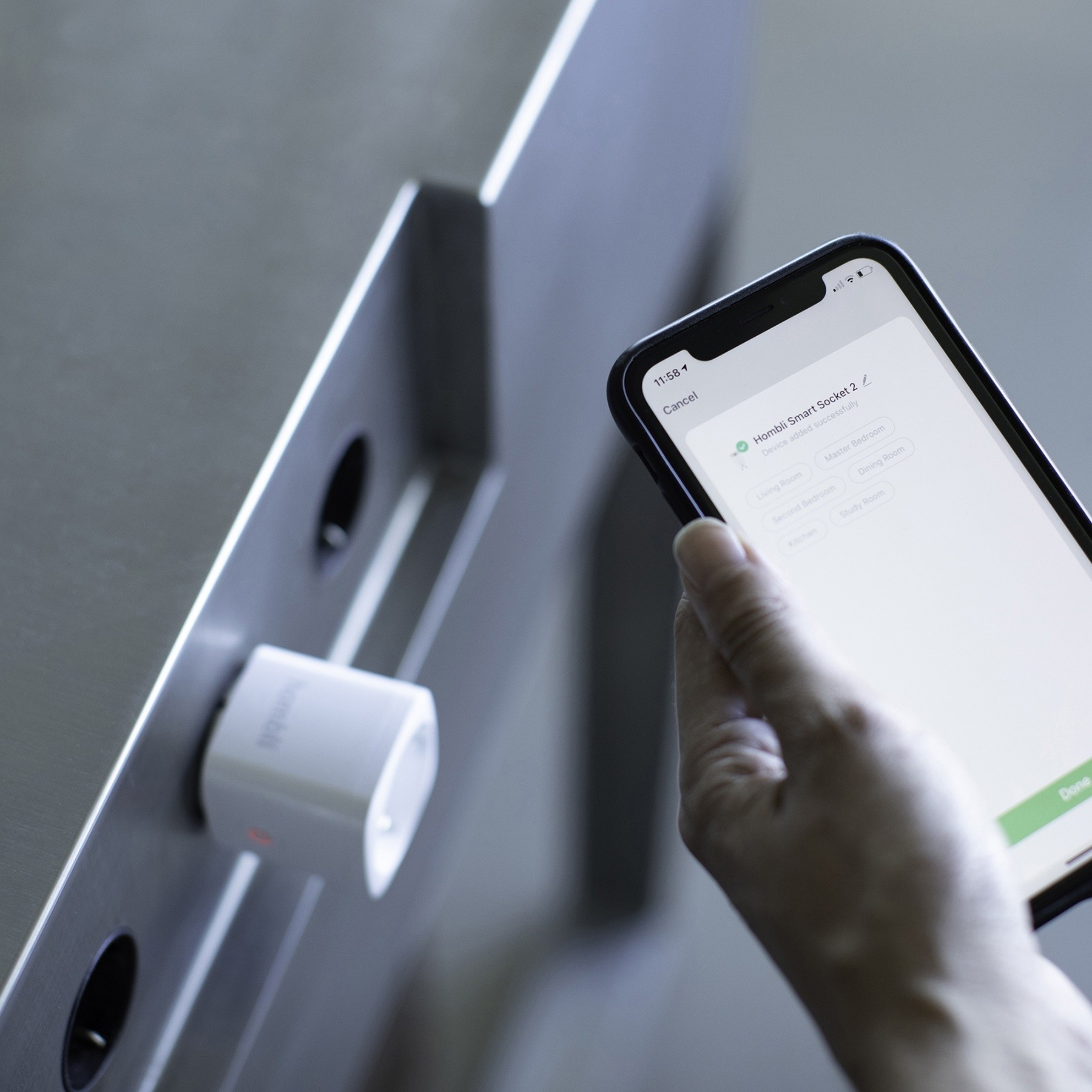 Prise intelligente à côté d'un téléphone affichant un réglage. Une personne tient le téléphone. La prise est blanche.