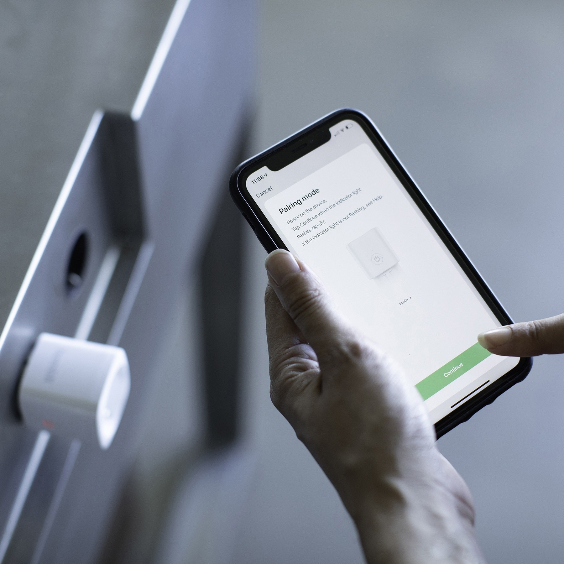 Une main tient un smartphone à côté d'une prise intelligente murale. Le téléphone affiche un écran de mode d'appairage.