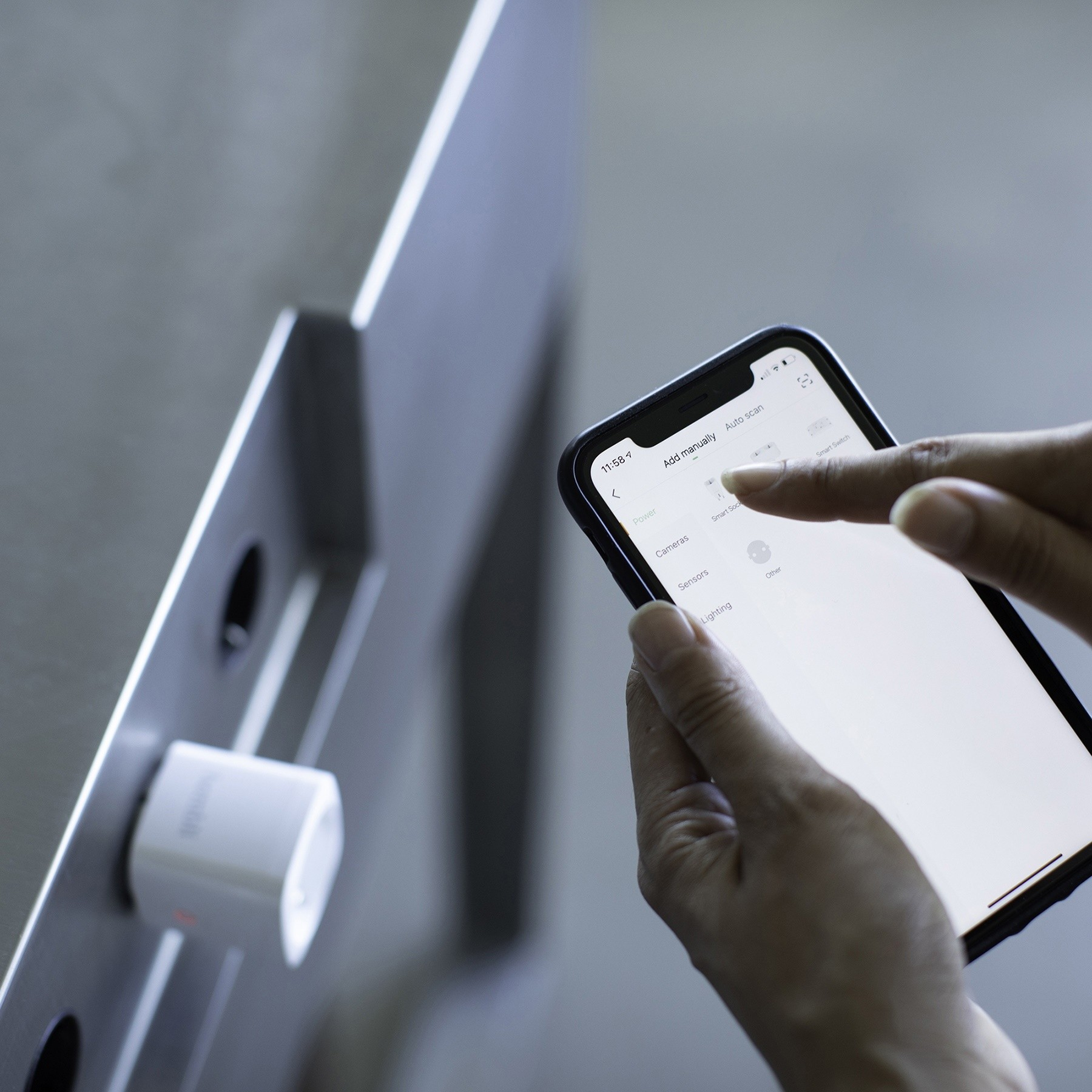 Les mains d'une personne utilisant un téléphone près d'un mur. Une prise intelligente est sur le mur.