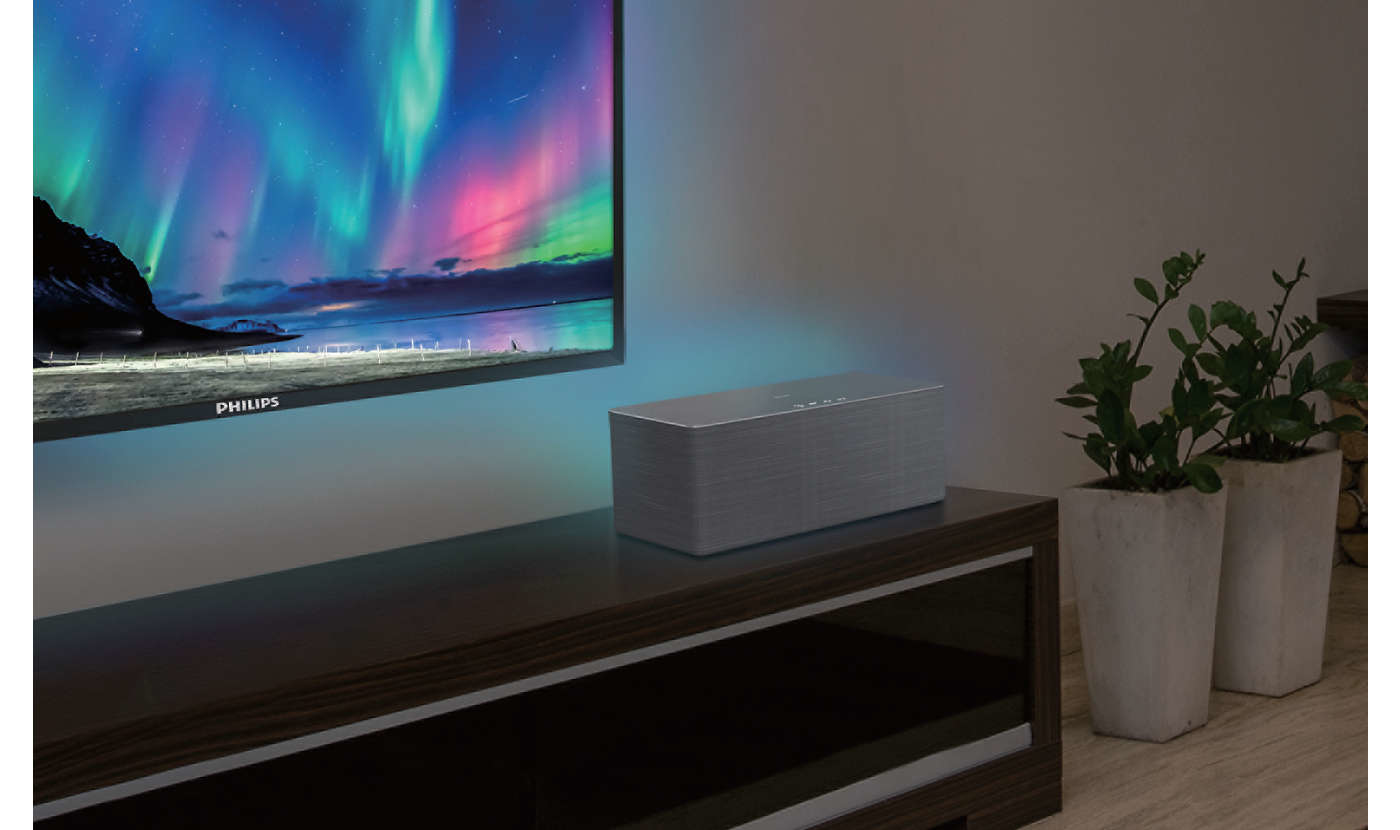 Eine Soundbar auf einem dunklen Schrank. Dahinter zeigt ein Fernseher eine Aurora.