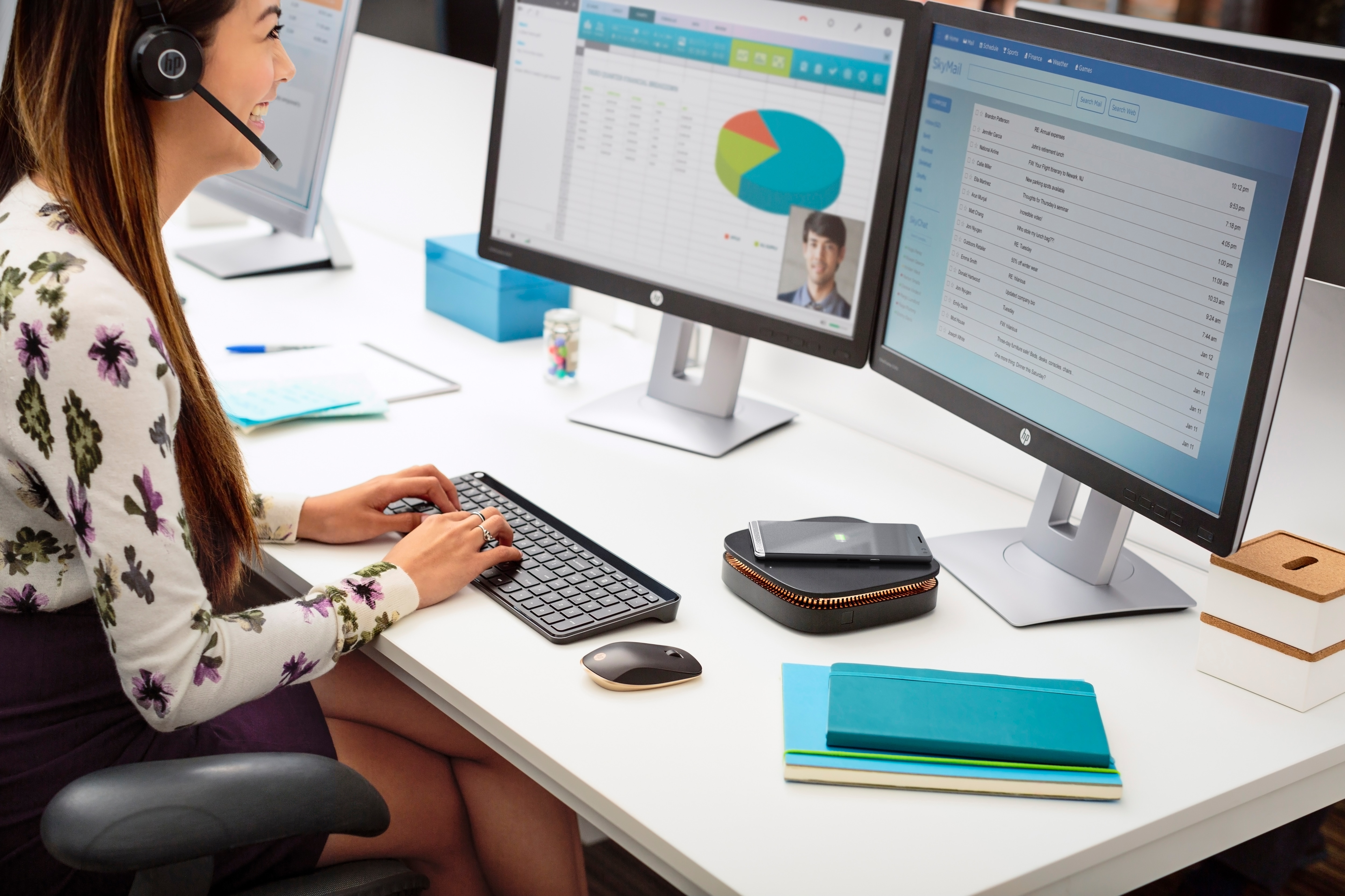 Frau arbeitet an mehreren Monitoren, trägt ein Headset, mit Büromaterial auf dem Schreibtisch.
