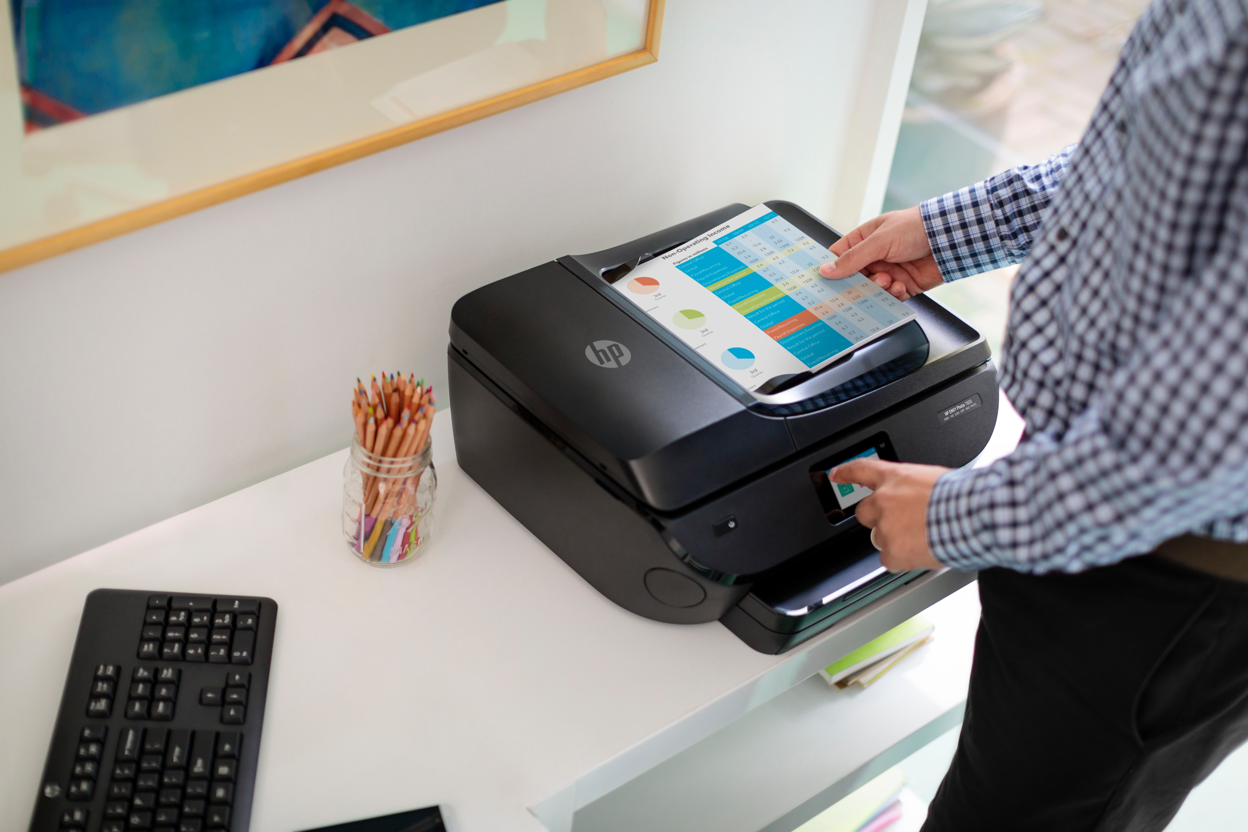 Eine Person, die einen schwarzen HP-Drucker auf einem weißen Schreibtisch mit Bleistiften und Tastatur benutzt.