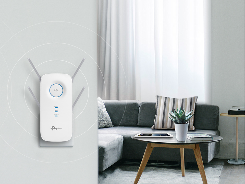 Fehér TP-Link WiFi jelerősítő a falon, háttérben kanapé, asztal, növény.