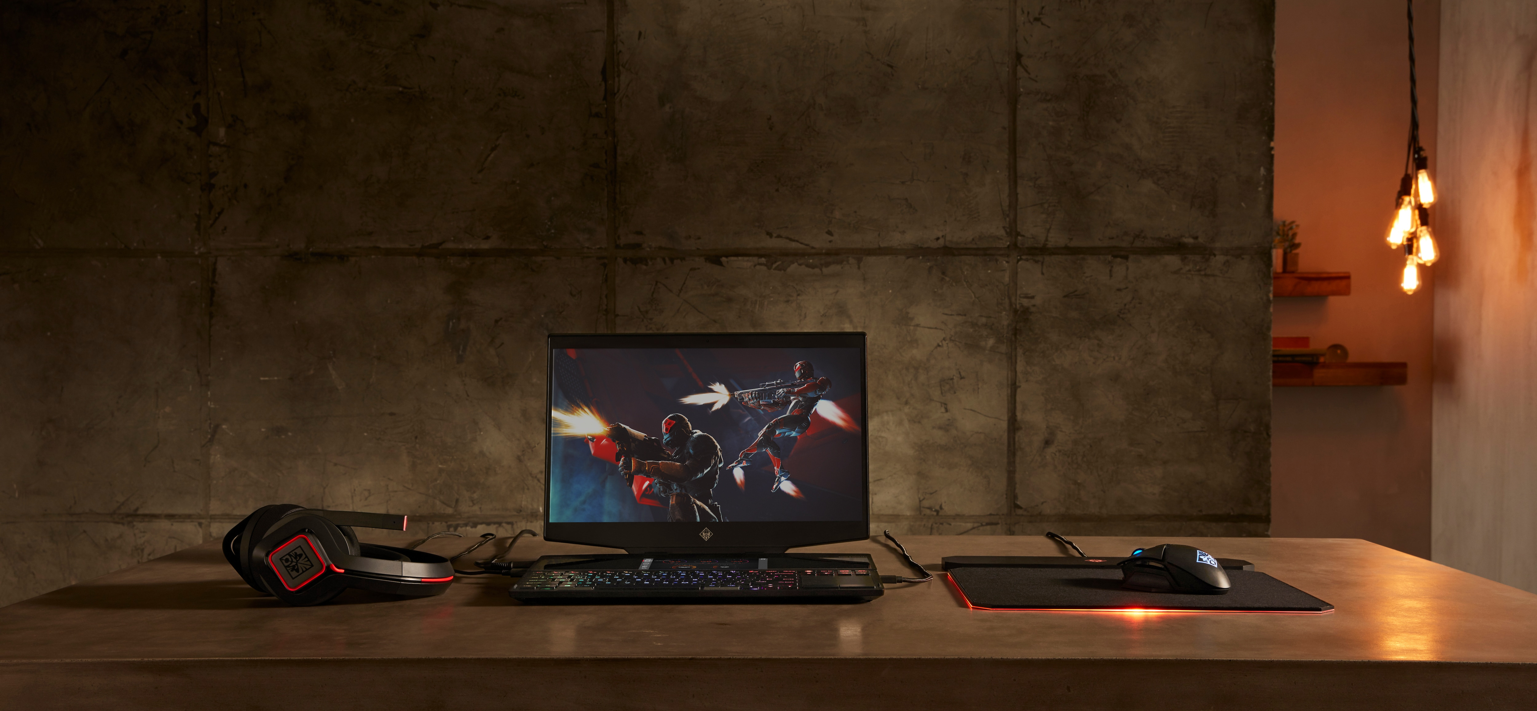 Configuración de juego: Laptop muestra escena de juego. Auriculares, ratón, alfombrilla y teclado en el escritorio.