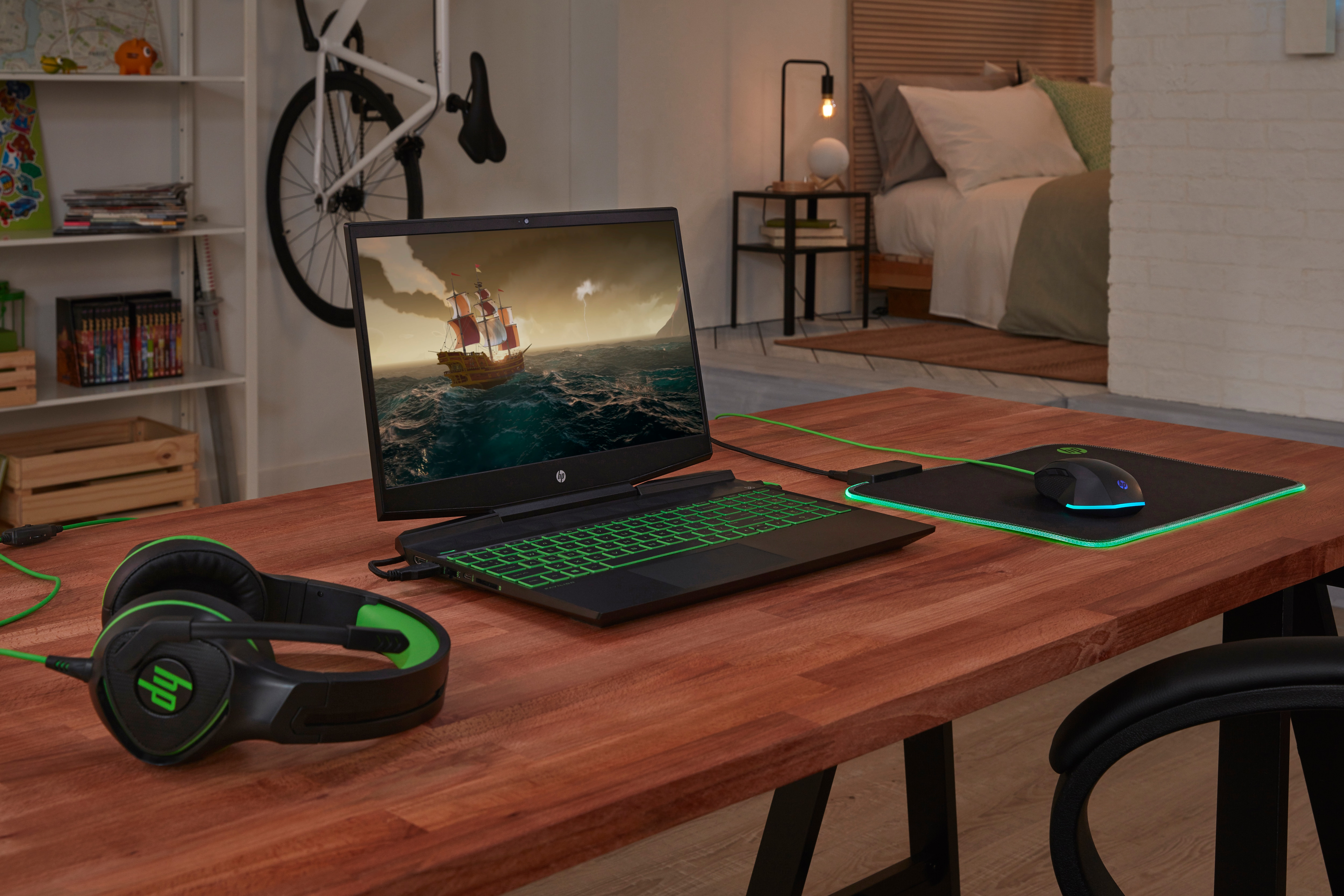 Gaming-Setup mit Laptop, Maus, Kopfhörern und Mauspad auf einem Holzschreibtisch. Schlafzimmerhintergrund.