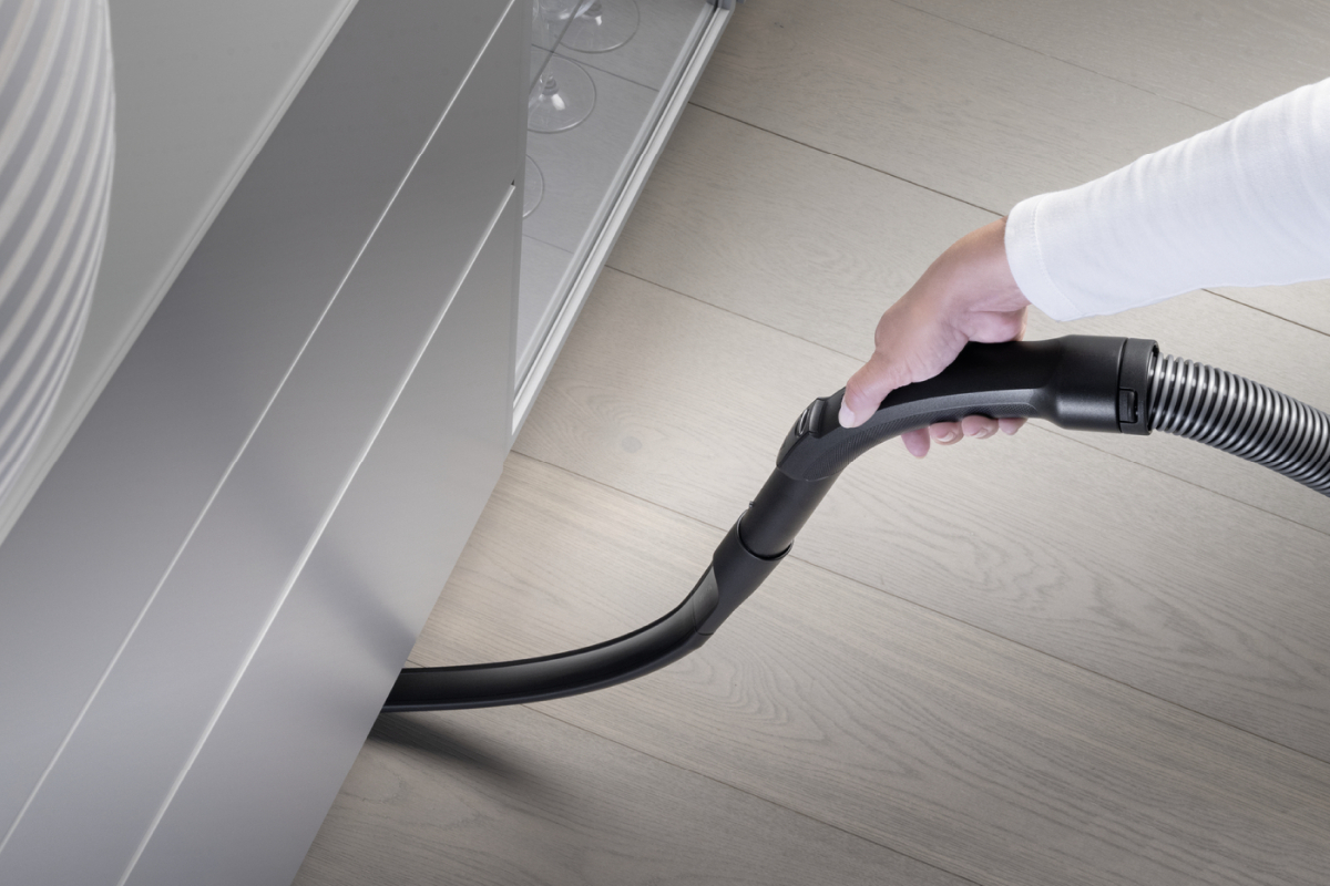 Eine Hand benutzt einen Staubsauger. Der Staubsauger ist schwarz und reinigt zwischen Schrank und Boden.