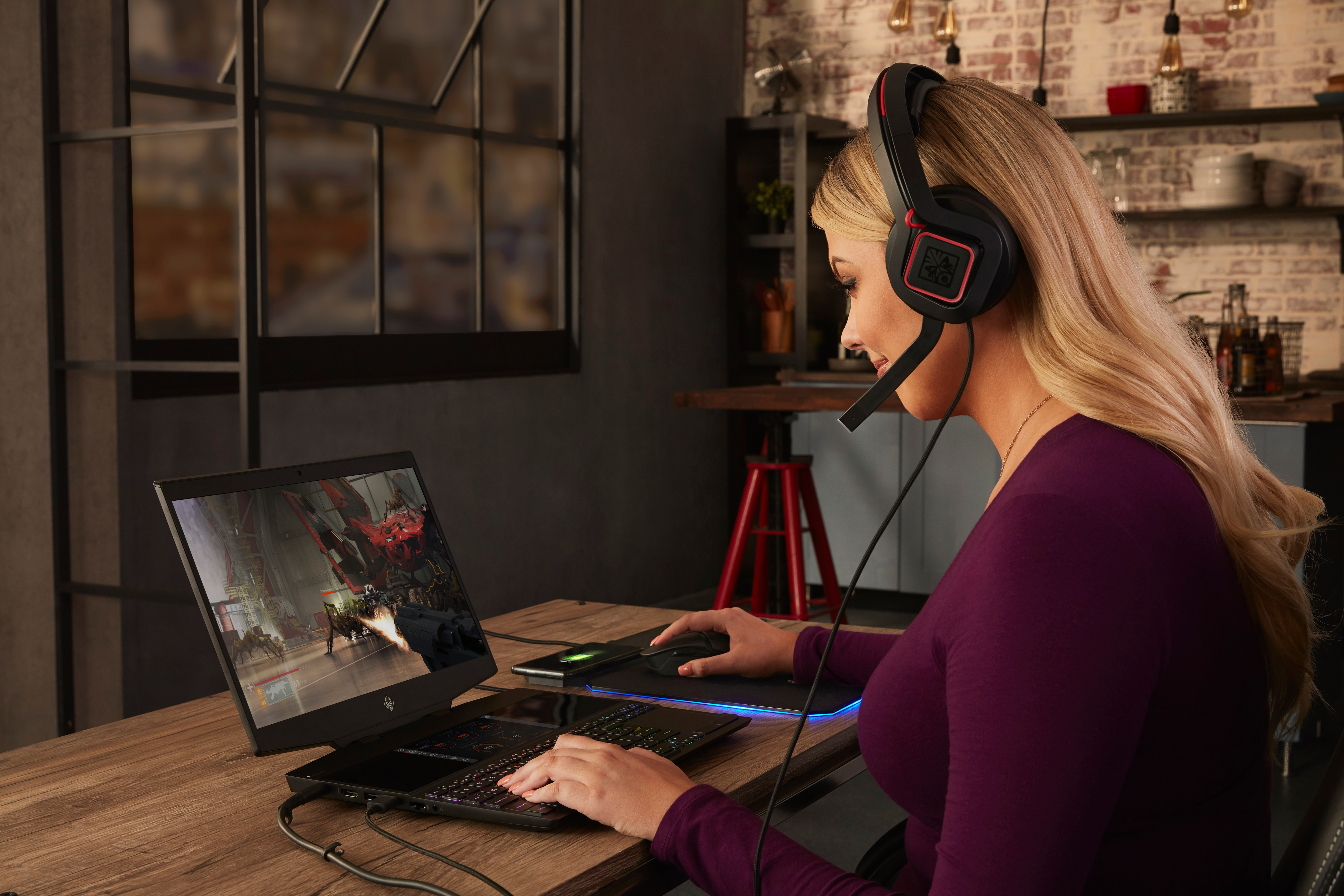 Mujer jugando en portátil con auriculares y ratón, en un entorno doméstico.