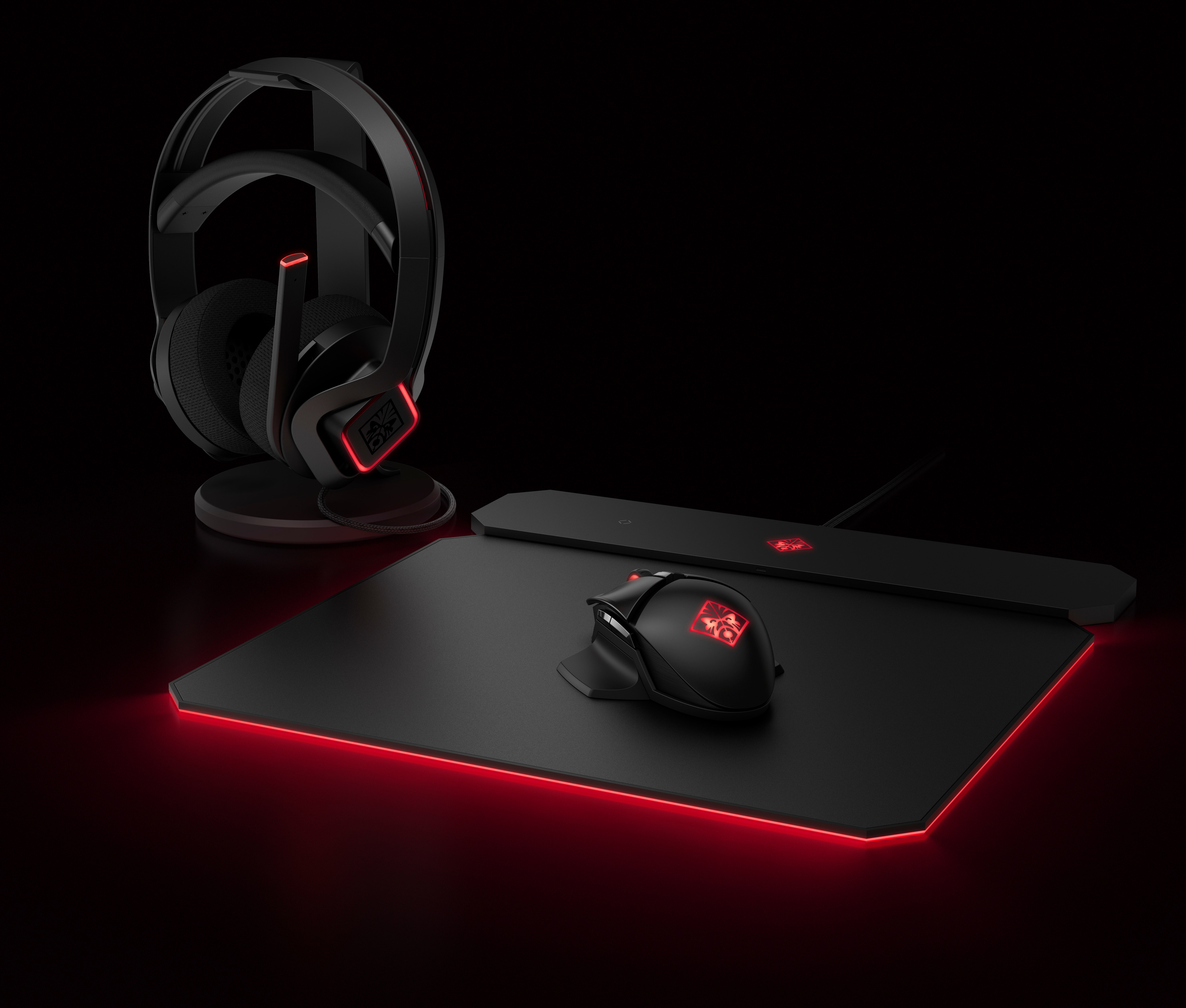 Una configuración de juego con auriculares, ratón y alfombrilla, todos con detalles rojos sobre un fondo negro.