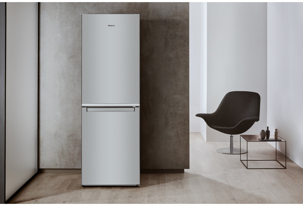 Een zilveren Whirlpool koelkast met een moderne stoel en tafel in een kamer.