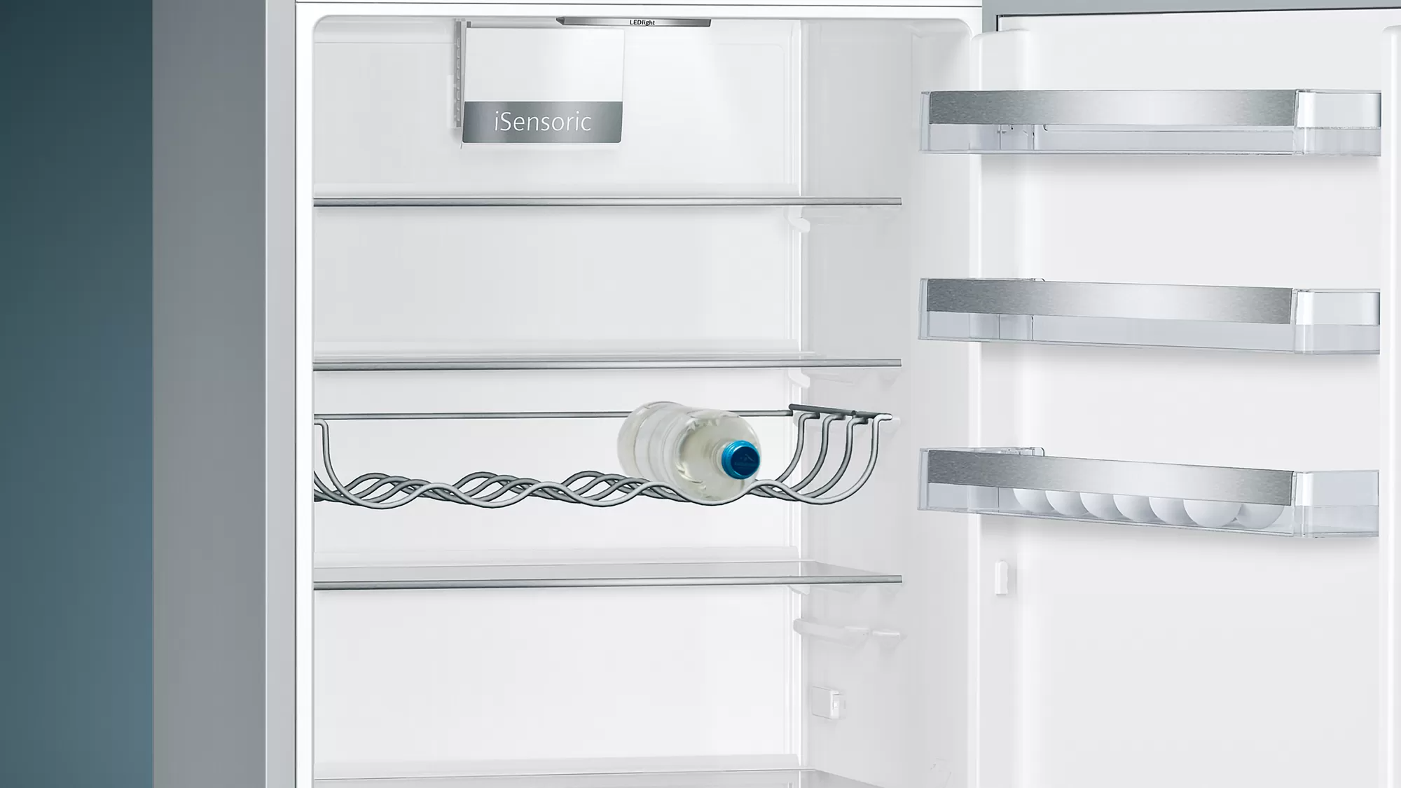 Open refrigerator interior. A bottle of water sits in a wire holder, shelves are visible.