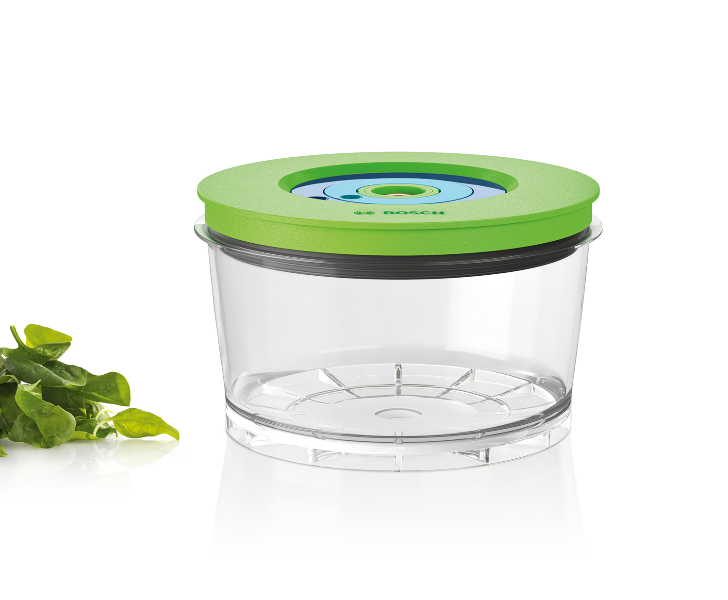 A clear plastic food container with a green lid and a few leaves of spinach.