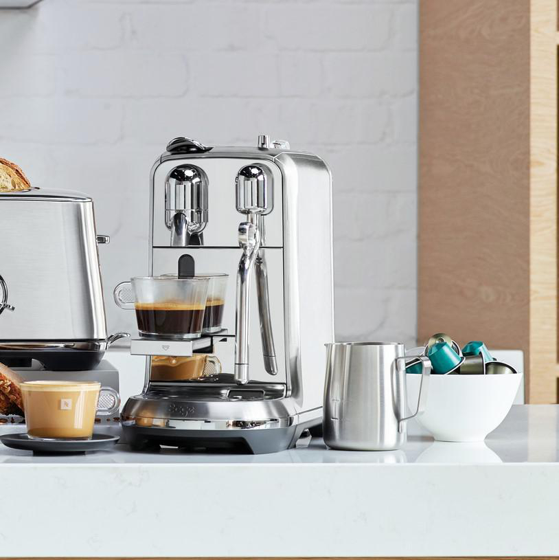 Espressomaschine aus Edelstahl mit zwei Tassen, einem Milchaufschäumer und Kaffeepads.