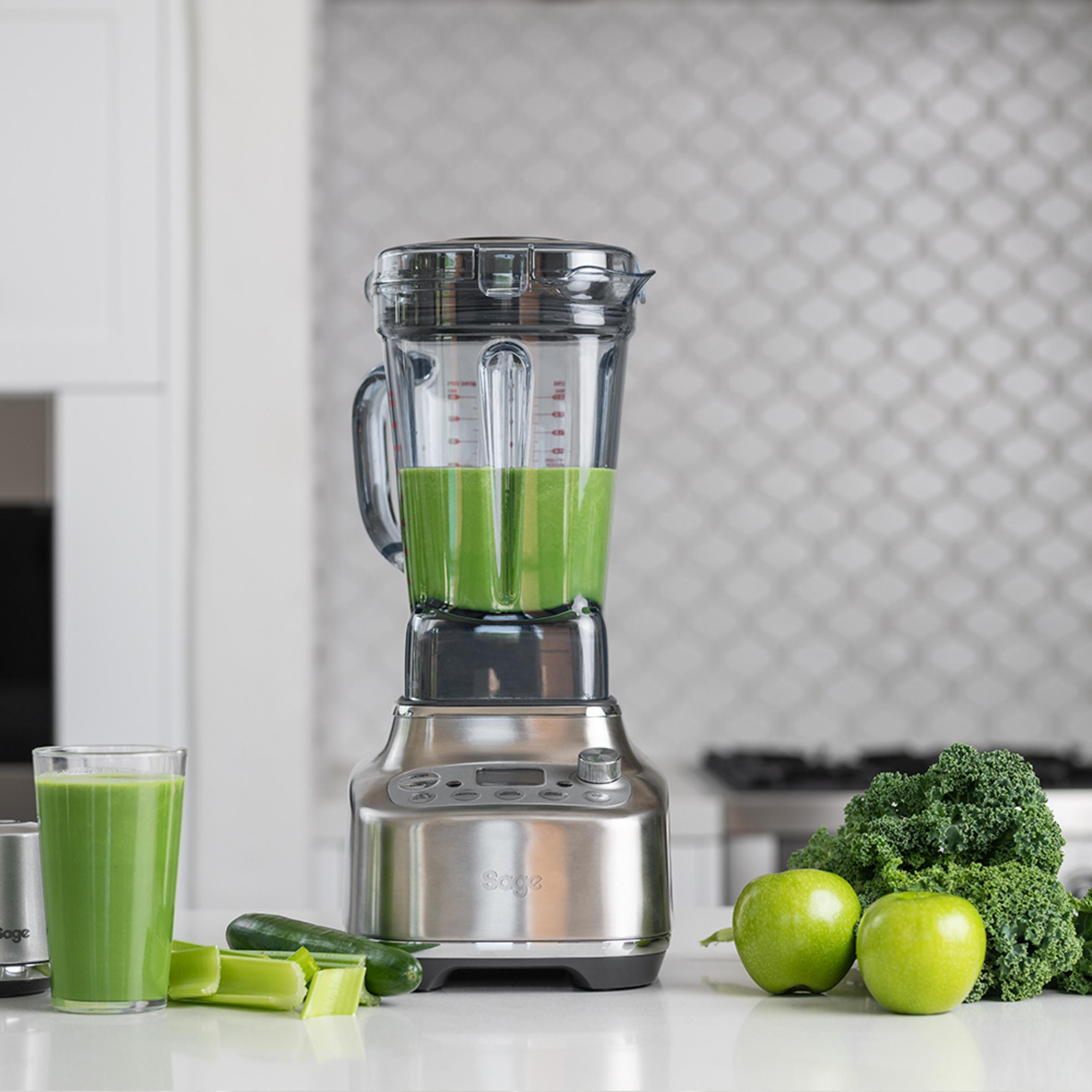 Ein Mixer mit grüner Flüssigkeit, Früchten und Zutaten.