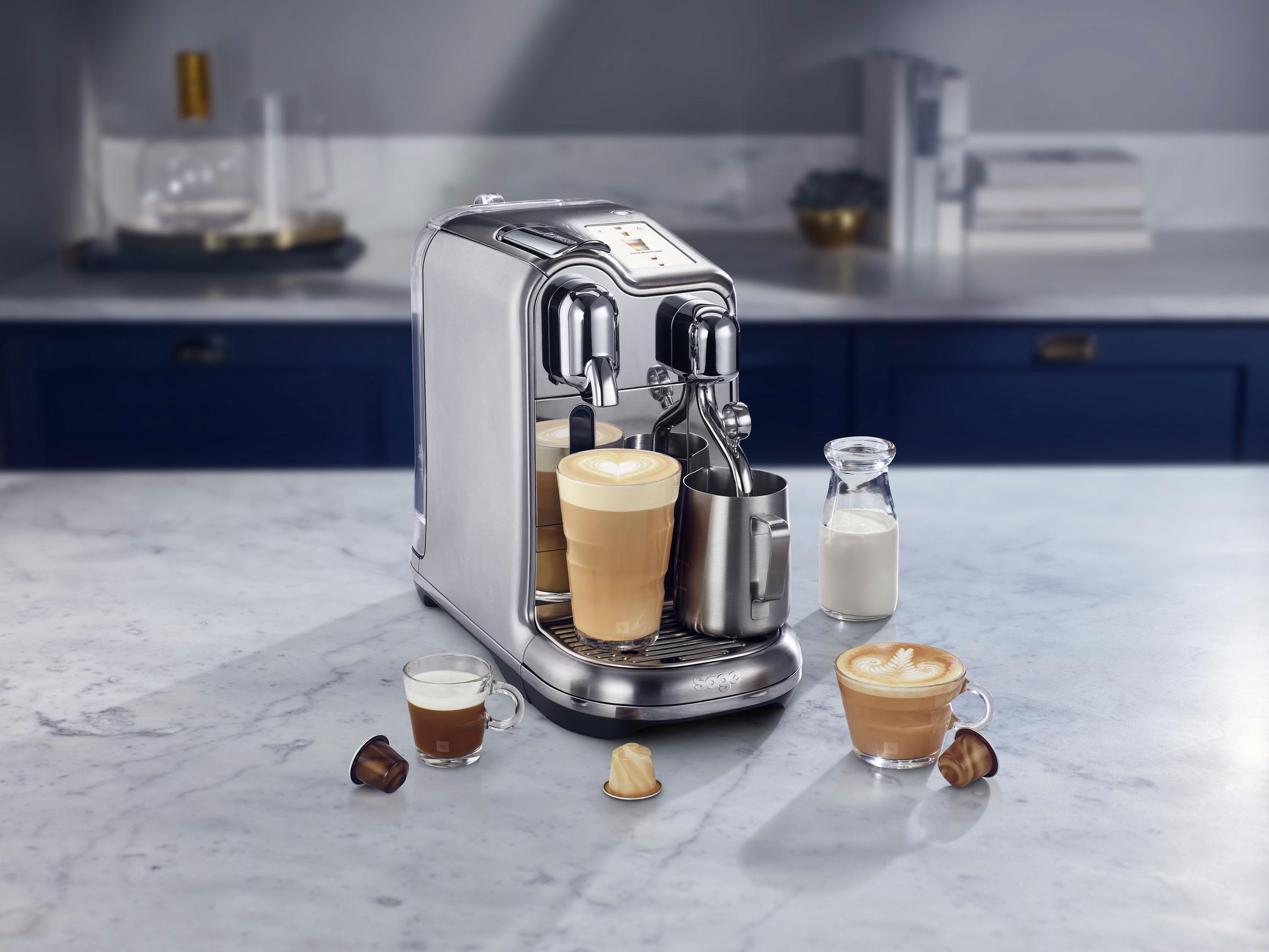 Silberne Kaffeemaschine mit zwei Gläsern, Milch und Kaffeekapseln.