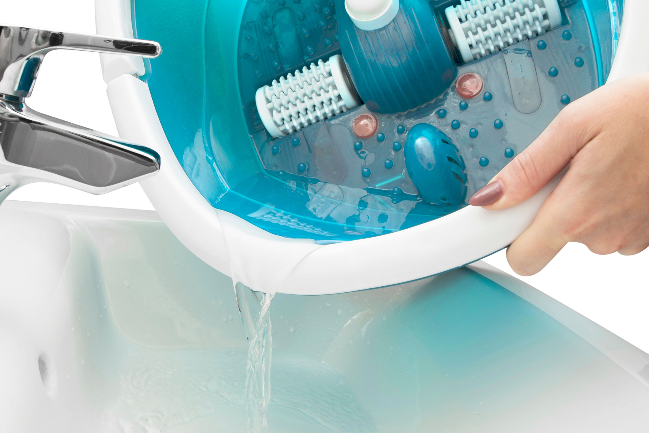 A person pours water from a blue foot spa into a white sink. The spa has rollers and a hand is holding it.