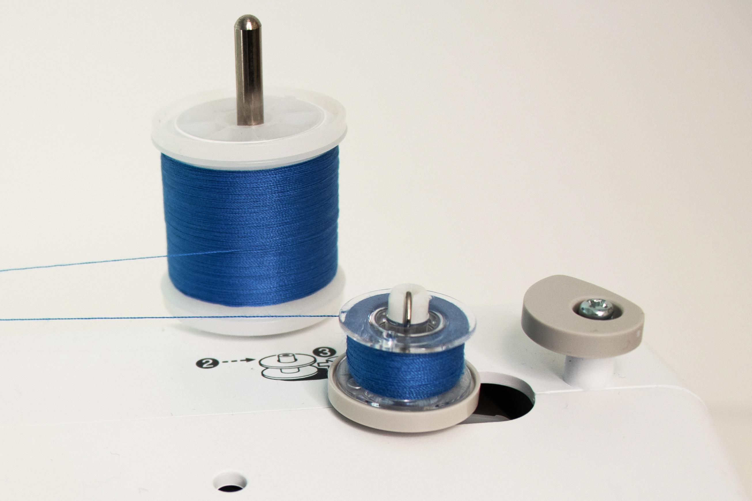Eine Nähmaschine mit blauer Garnrolle und kleiner Spule.
