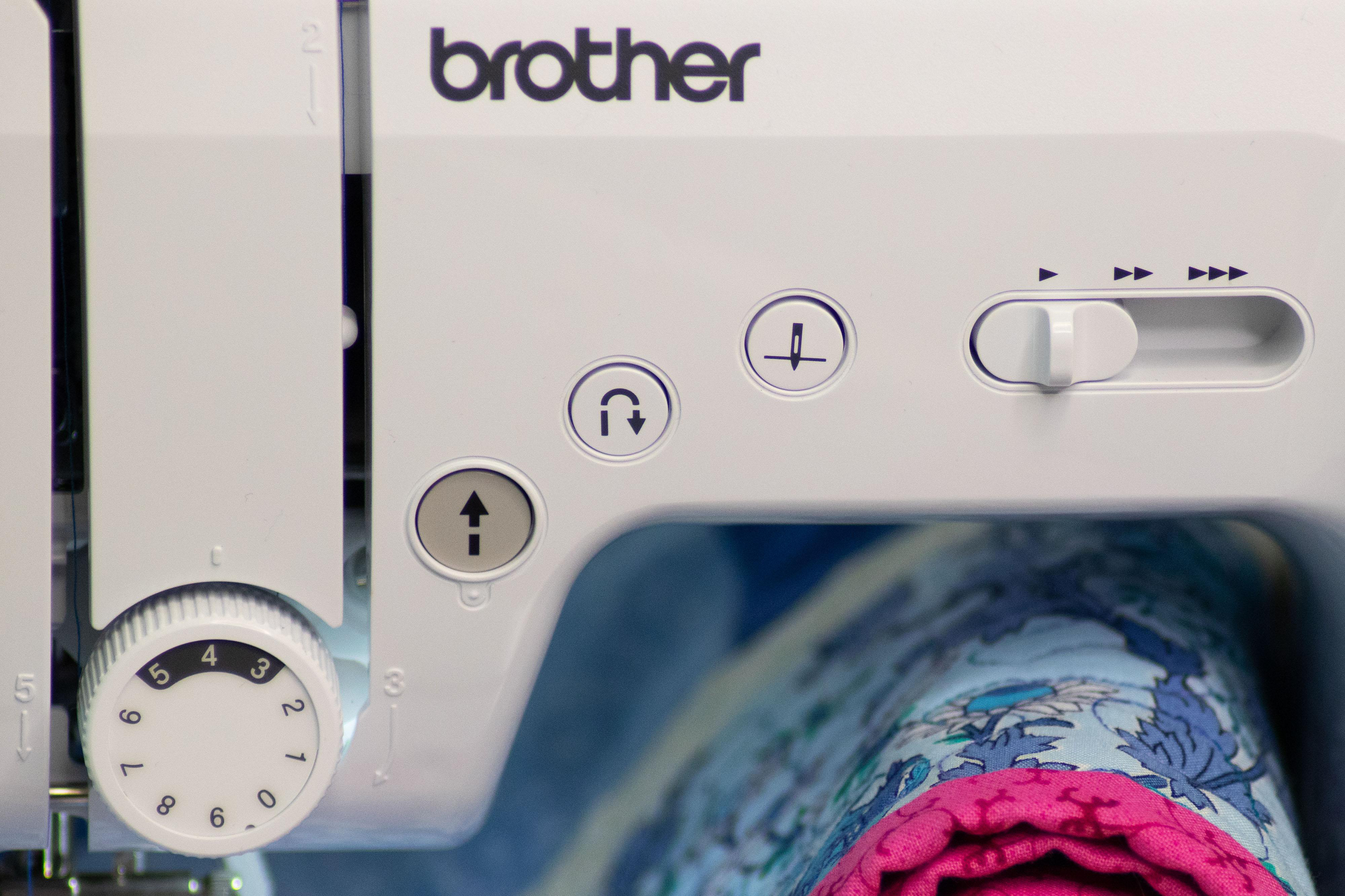 Nahaufnahme der Vorderseite einer Brother-Nähmaschine mit Bedienelementen, Knöpfen und Stoff.