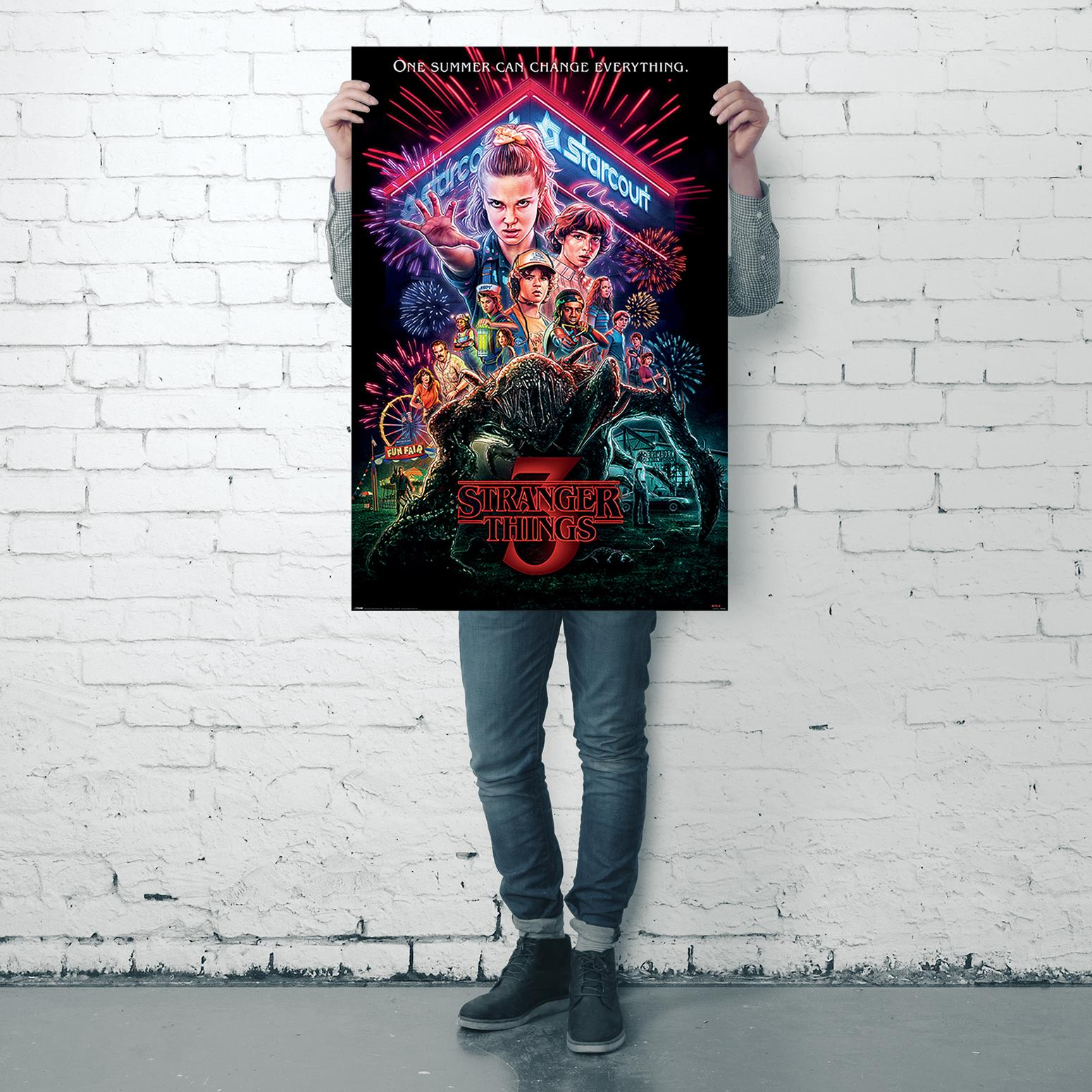 Person hält ein Poster von 'Stranger Things' mit mehreren Charakteren und Feuerwerk.