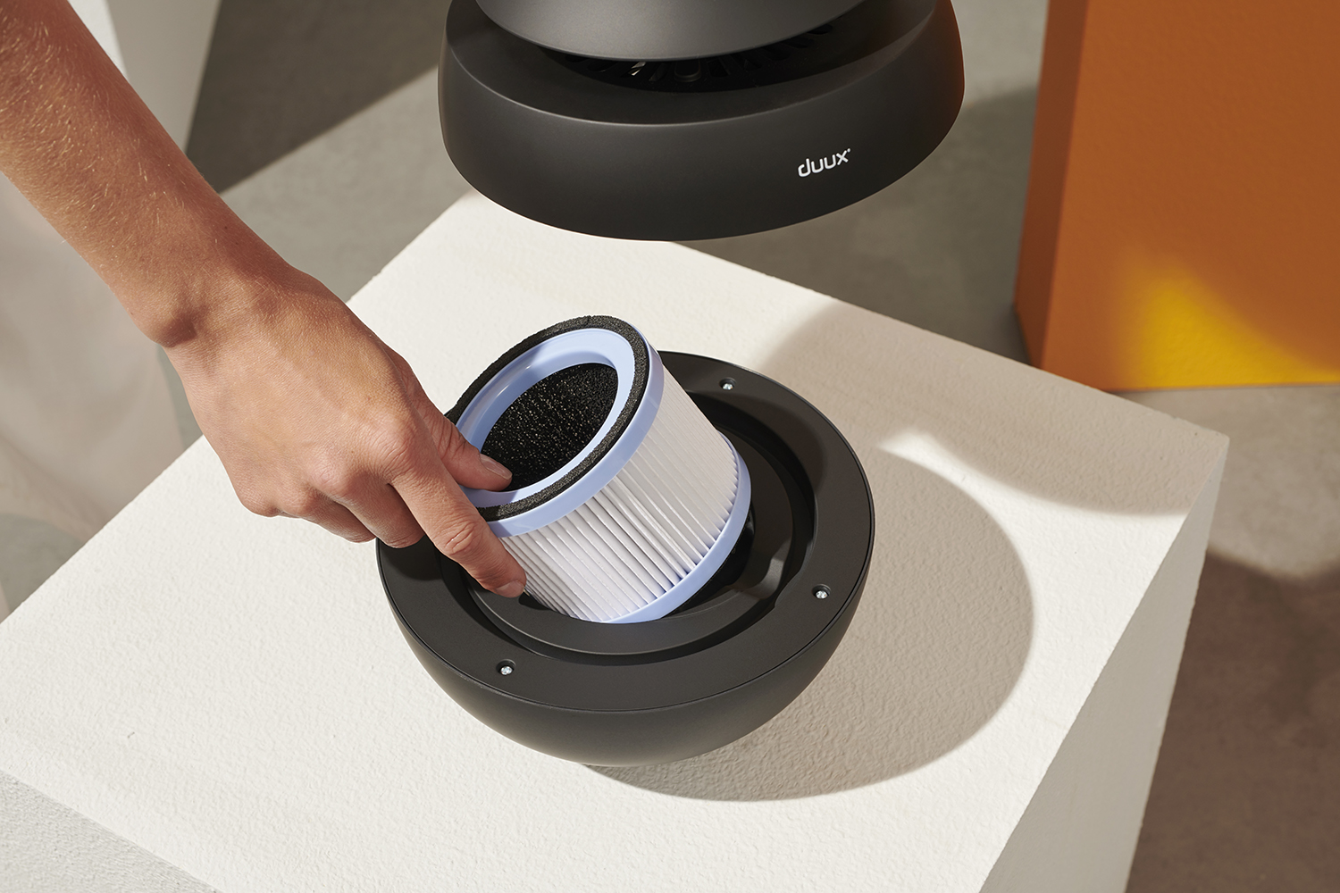 A hand replacing an air purifier filter into a black, spherical base.