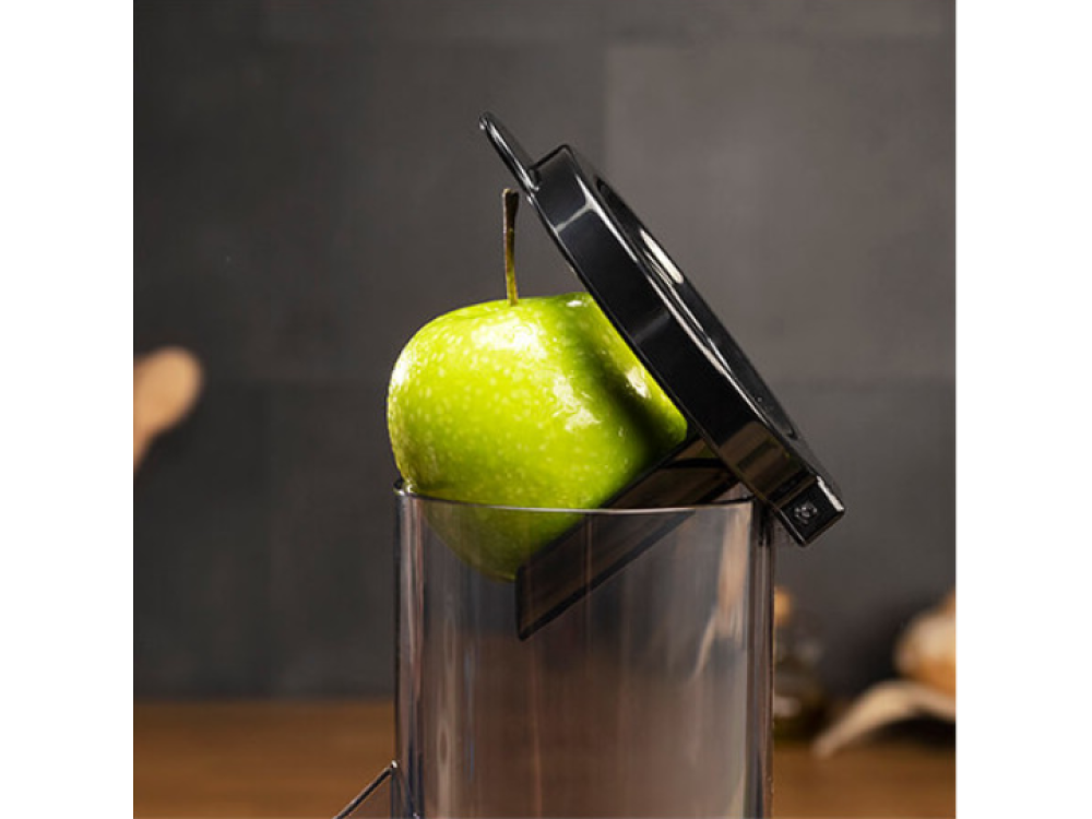 Una manzana verde siendo cortada. Un recipiente transparente es visible. El cortador es negro.