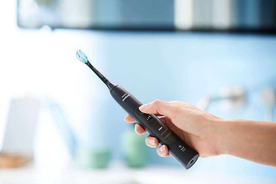 Une personne tenant une brosse à dents électrique noire. La brosse a des boutons et une tête de brosse bleue.