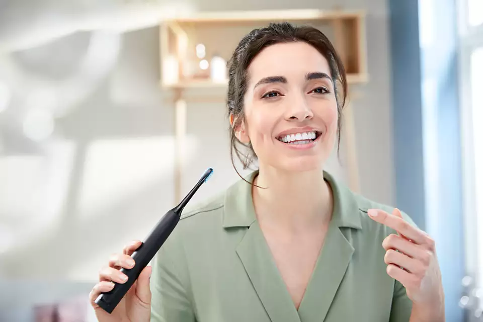 Femme tenant une brosse à dents noire, souriant à la caméra.