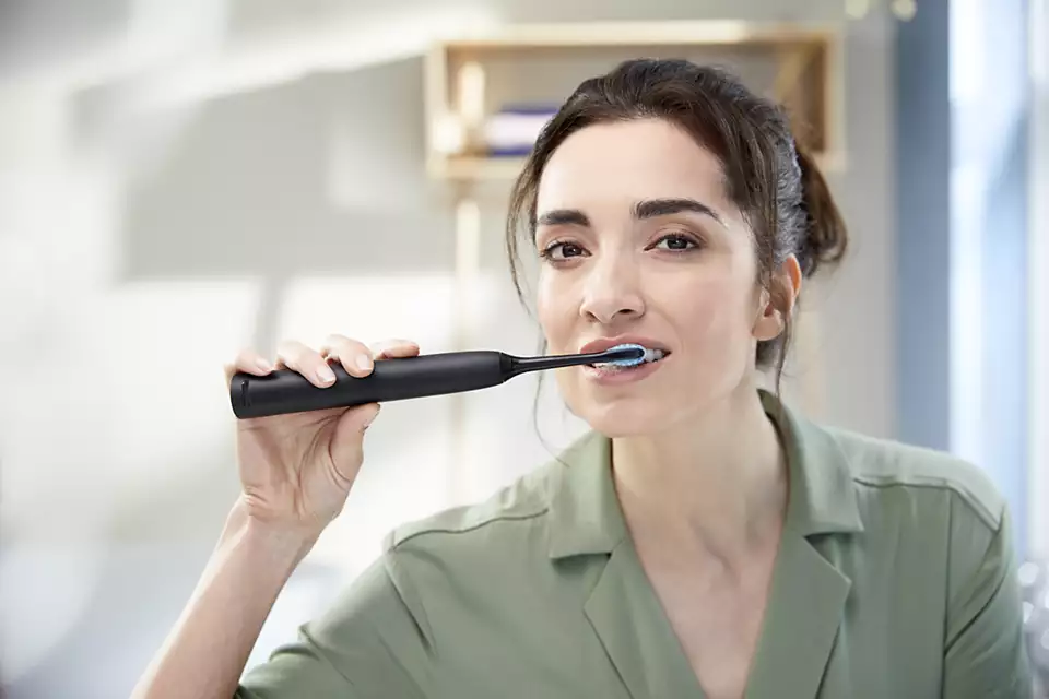 Une femme se brosse les dents avec une brosse à dents électrique noire.