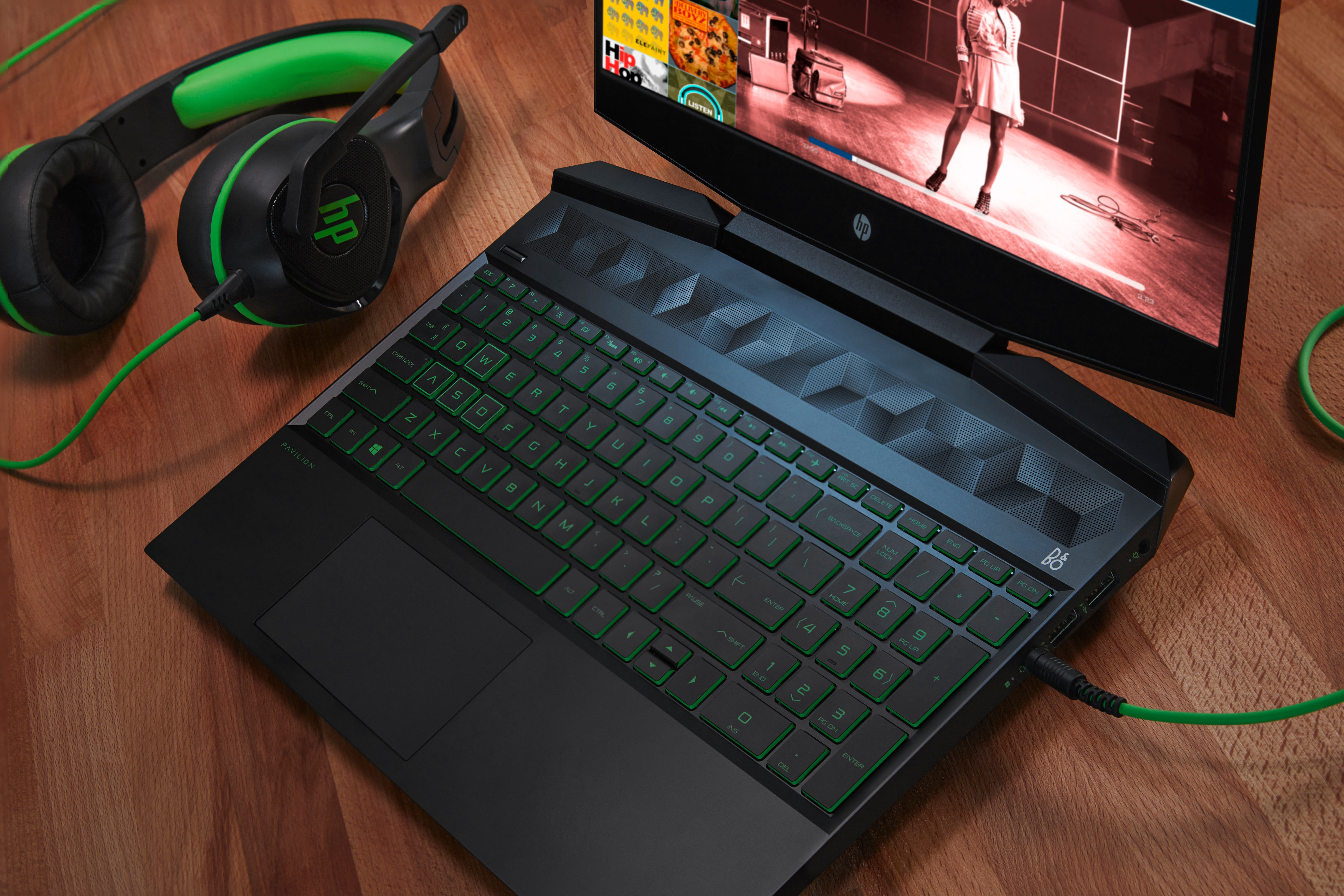 Laptop mit grün beleuchteter Tastatur und Headset auf einem Holztisch.