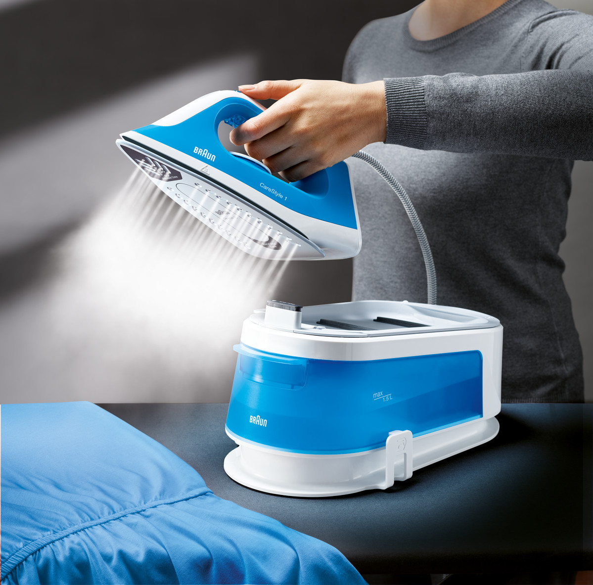 A person ironing with a blue Braun iron, steaming over a blue sheet on a dark surface.