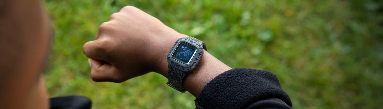 Handgelenk mit Smartwatch, die eine digitale Anzeige zeigt, inmitten von Grün.