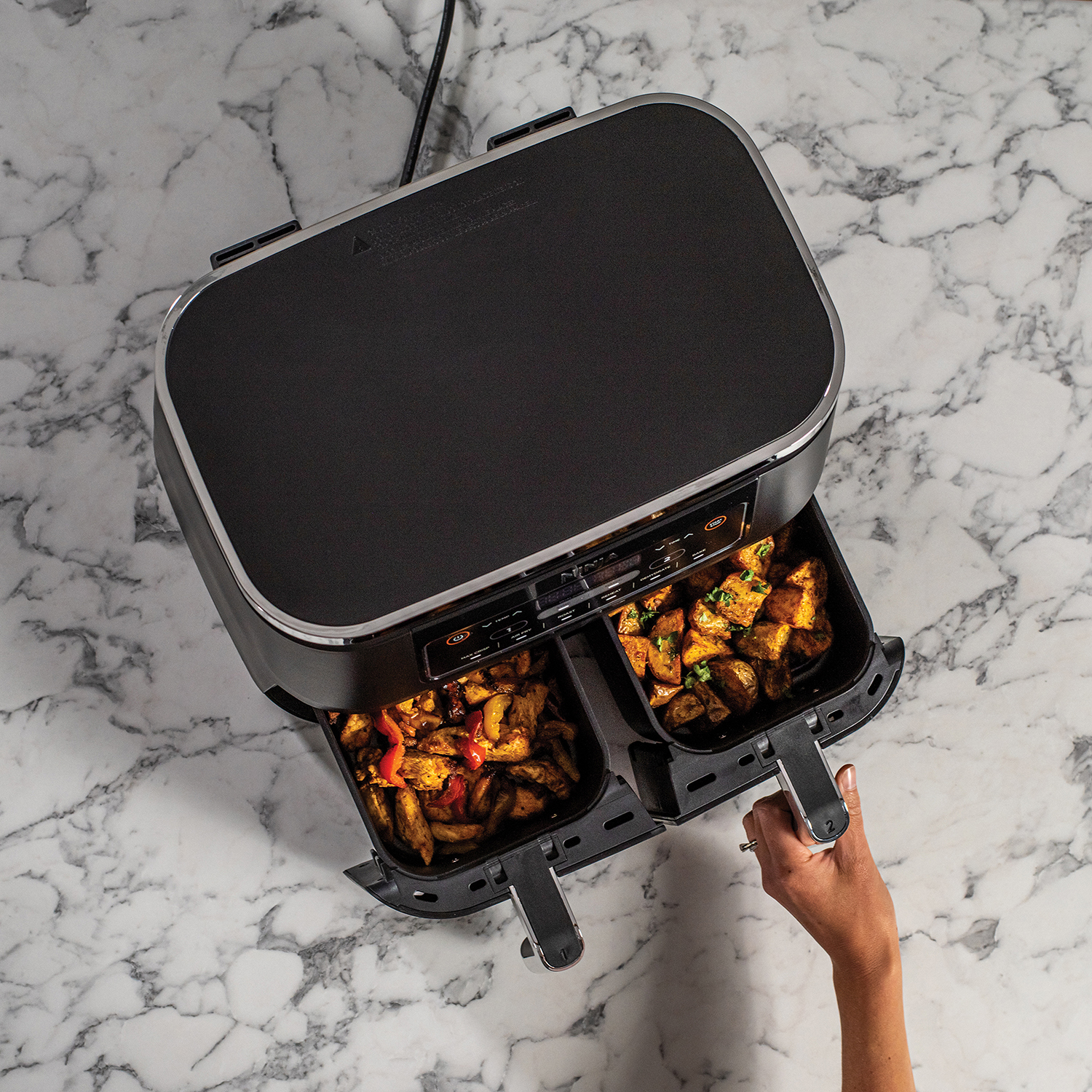 Een airfryer met twee manden vol eten. Een hand reikt naar één mand.
