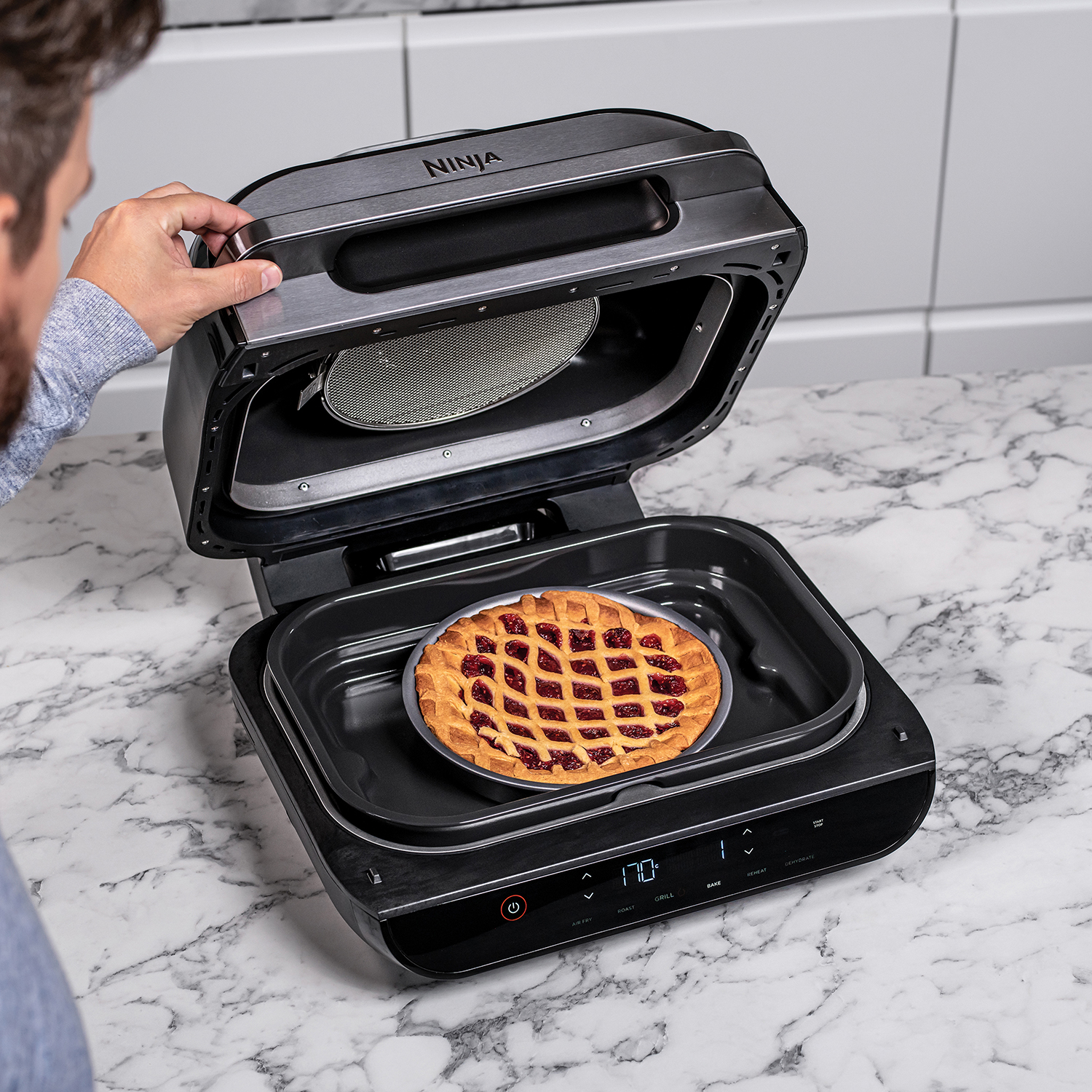 A Ninja Foodi oven with a pie inside. A man's hand is opening the oven.
