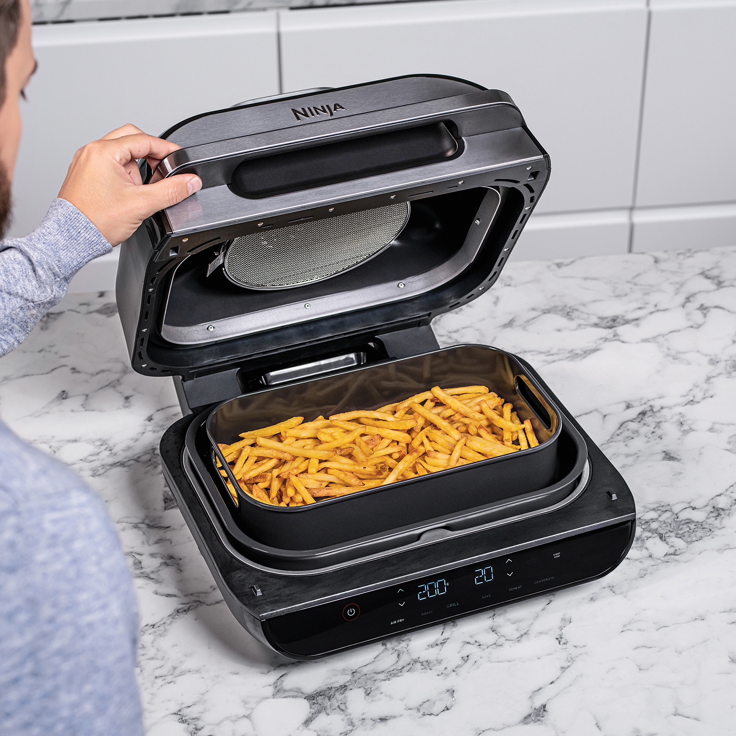 Person opening a Ninja grill with fries inside.