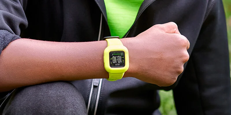 Le poignet d'une personne avec une montre intelligente jaune affichant l'heure. Herbe verte en arrière-plan.