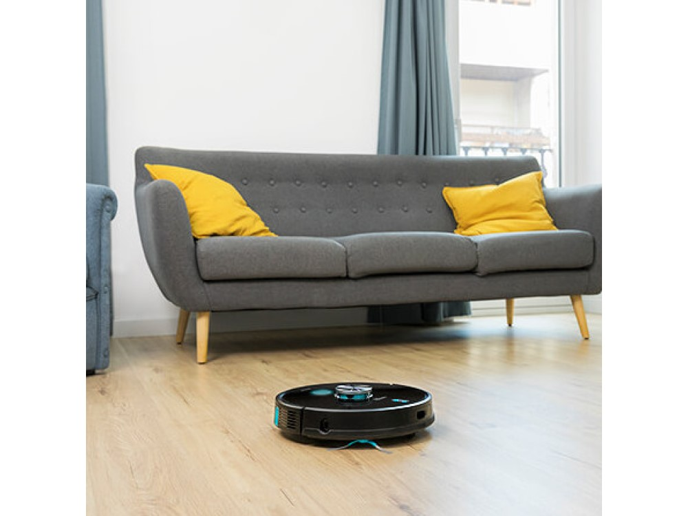 Una aspiradora robot en un piso de madera, con un sofá gris al fondo.