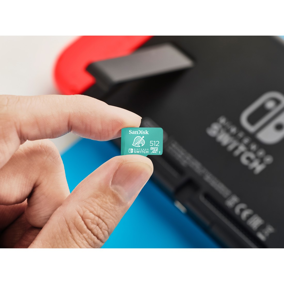 Eine Hand, die eine grüne, blaue und weiße Sandisk Micro-SD-Karte neben einer Nintendo Switch-Konsole hält.