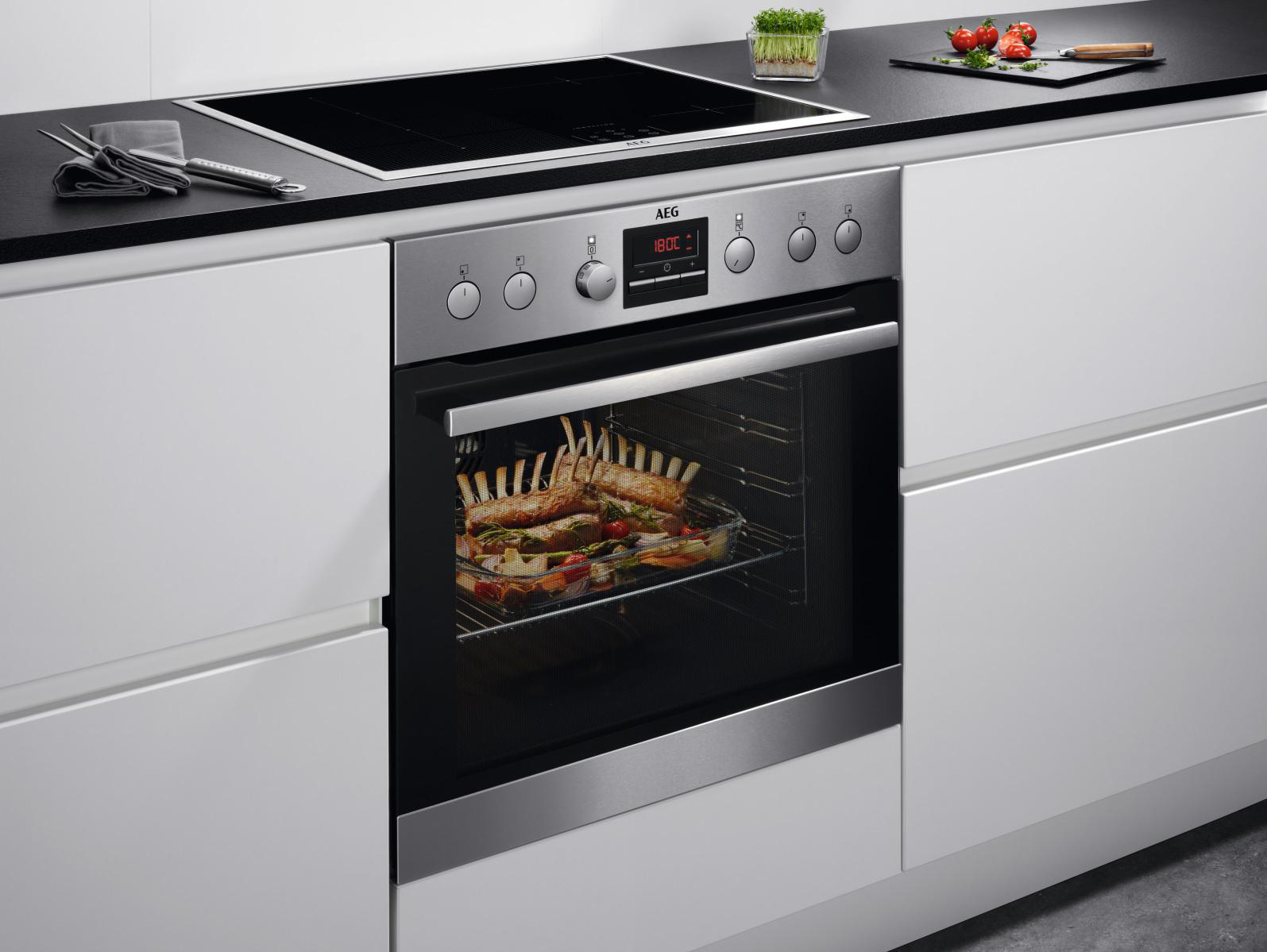 Ein Edelstahl-Backofen in einer weißen Küche, mit einem Braten im Inneren. Der Ofen ist an.