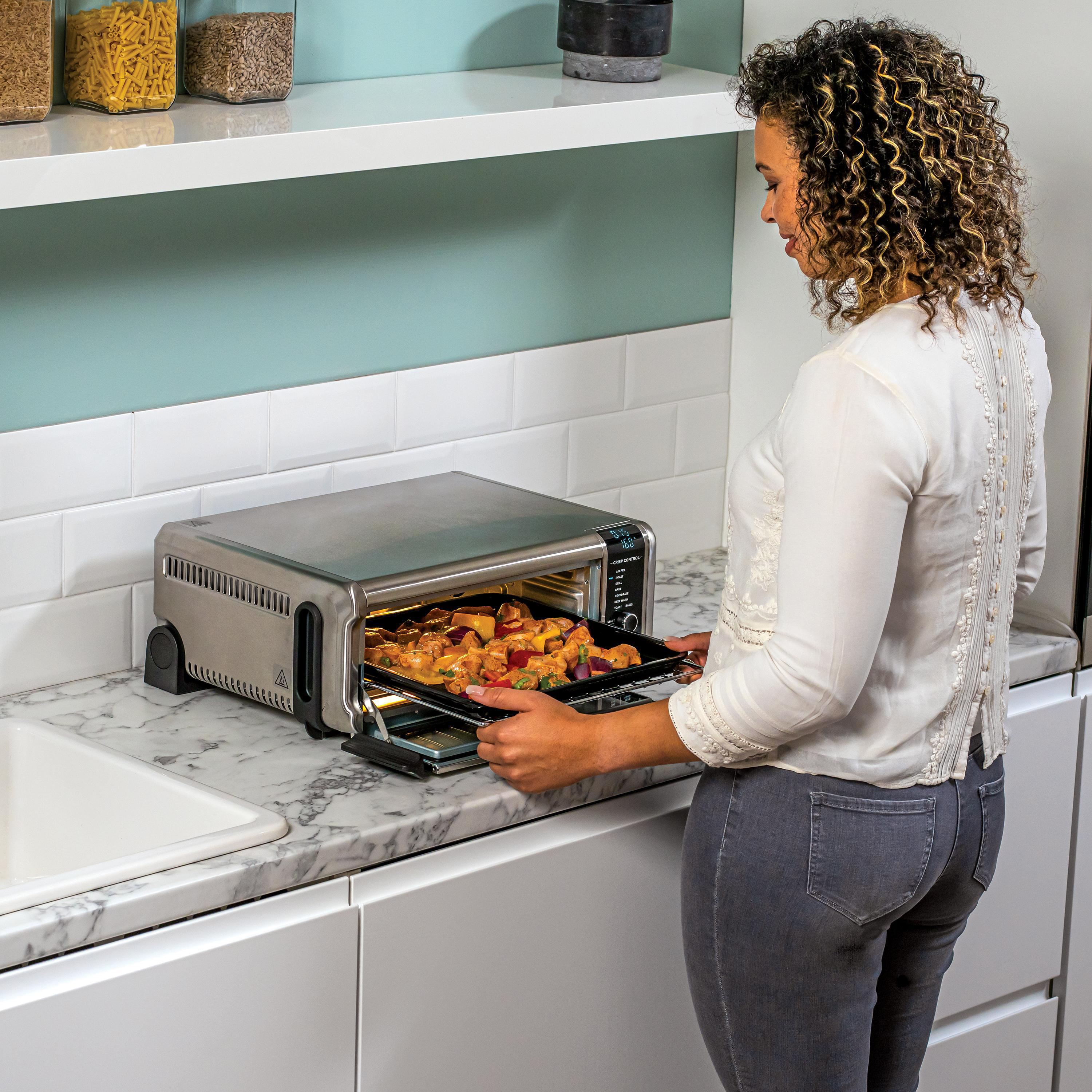Frau nimmt ein Tablett mit Essen aus einem silbernen Toaster-Ofen.