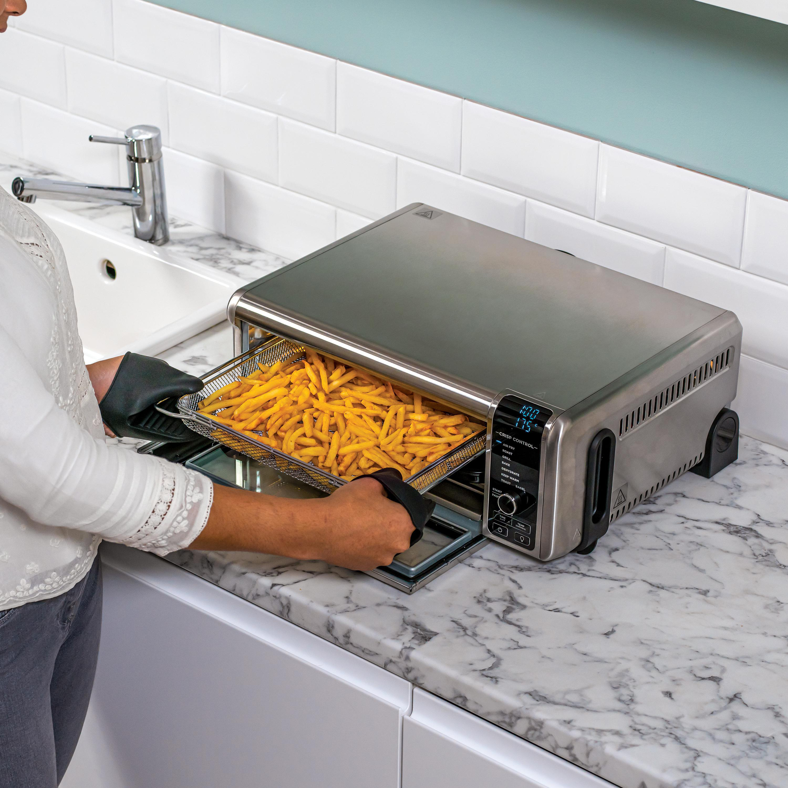 Silberner und schwarzer Heißluftfritteusen-Ofen mit Pommes Frites und einer Person mit Ofenhandschuhen.