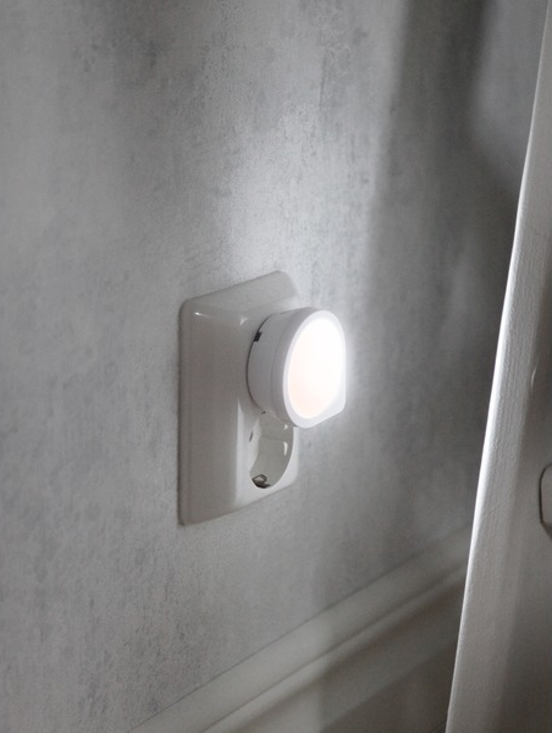Una luce notturna bianca collegata a una presa a muro. È illuminata, con una luce soffusa.