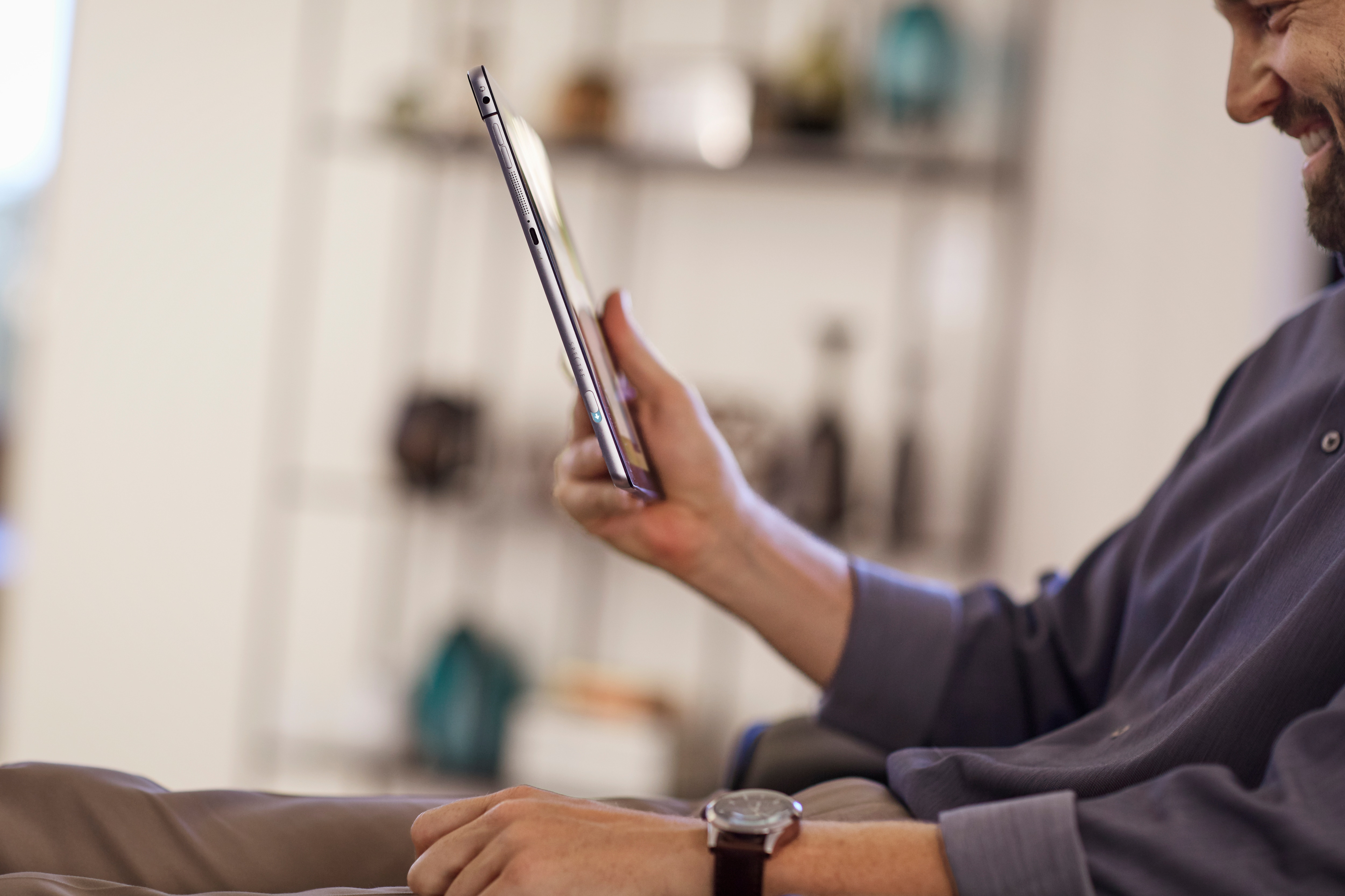 Ein Mann sitzt in einem Raum und hält ein Tablet in der Hand, während er lächelt.