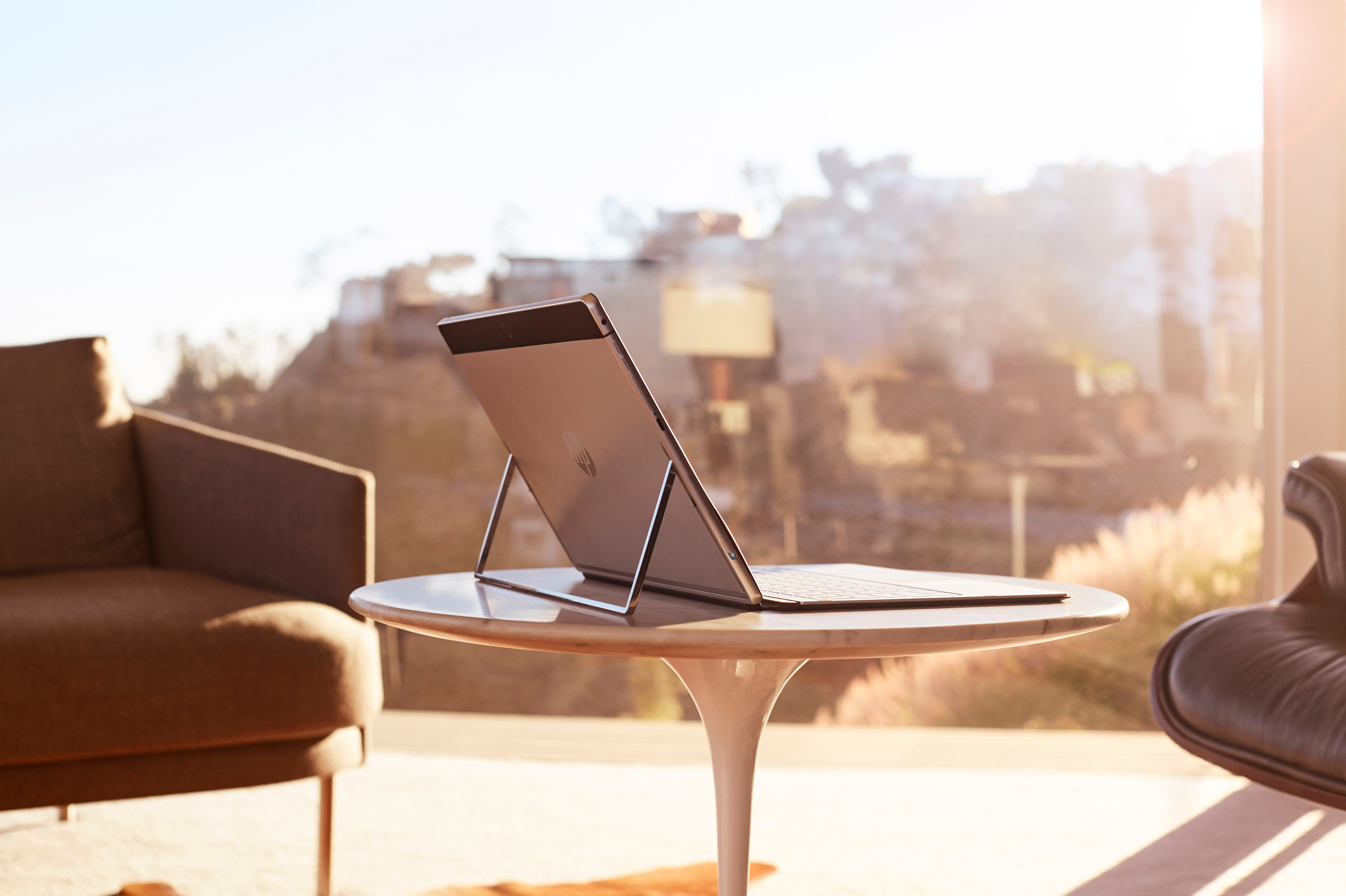 Ein Tablet mit ausgeklapptem Ständer steht auf einem runden Tisch in einem sonnigen Raum mit Sesseln und Aussicht.