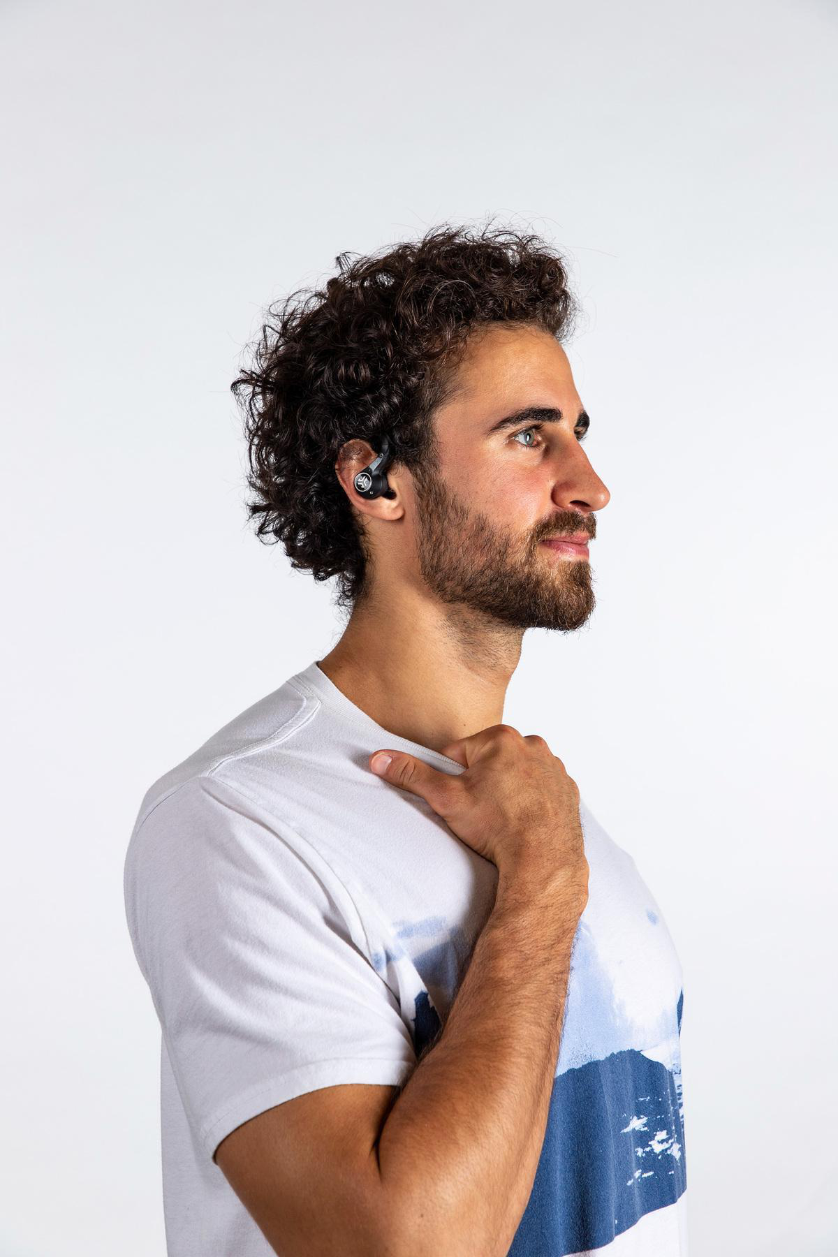 Ein Mann mit lockigem Haar, der ein weißes T-Shirt trägt, hat einen Ohrhörer in einem Ohr.