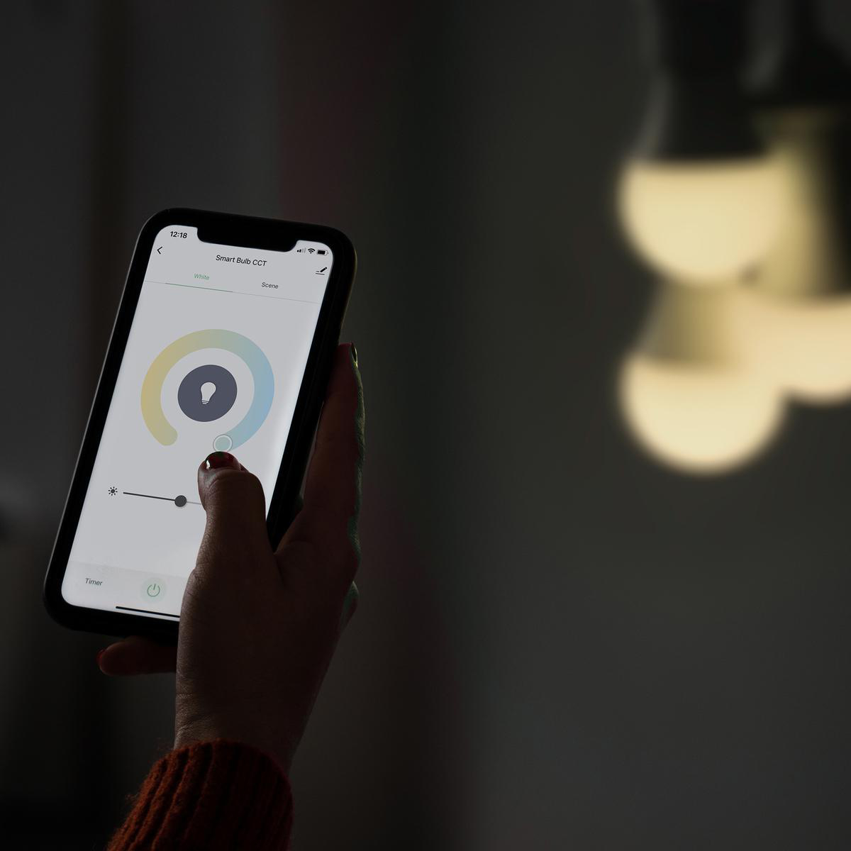 Eine Hand, die ein Smartphone mit einer Smart-Bulb-App und einem Glühbirnen-Symbol hält.